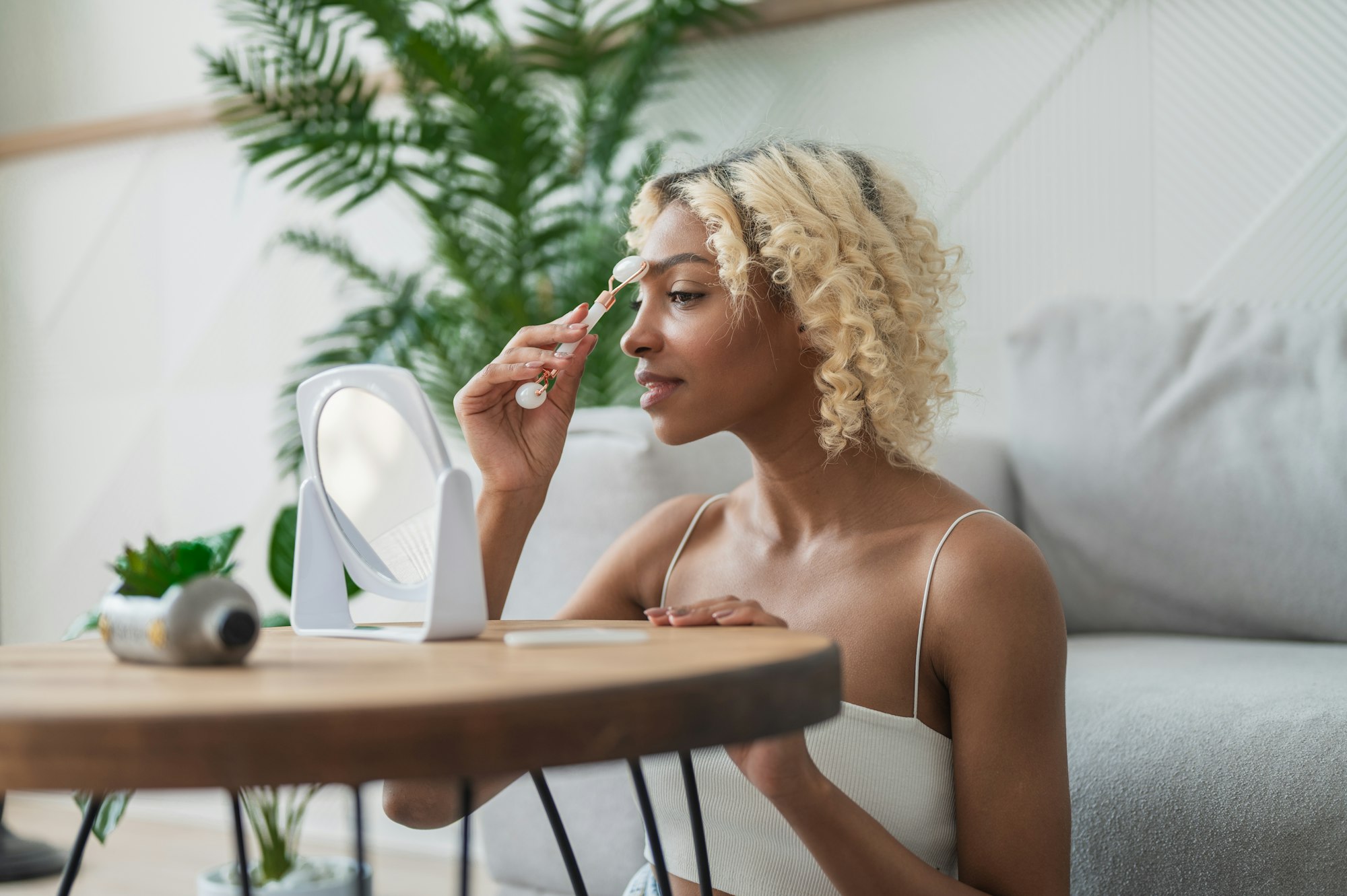 Side view on african american girl doing skin treatment at home. Woman using jade roller for skin