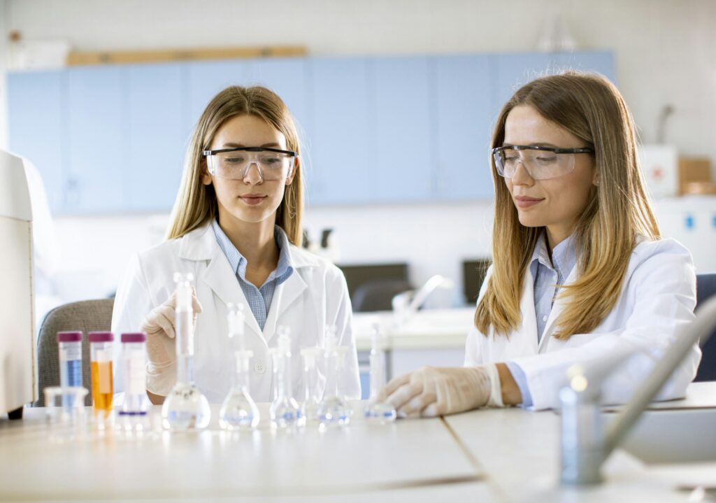 Two female scientific researchers looking at a flasks with solutions in a laboratory