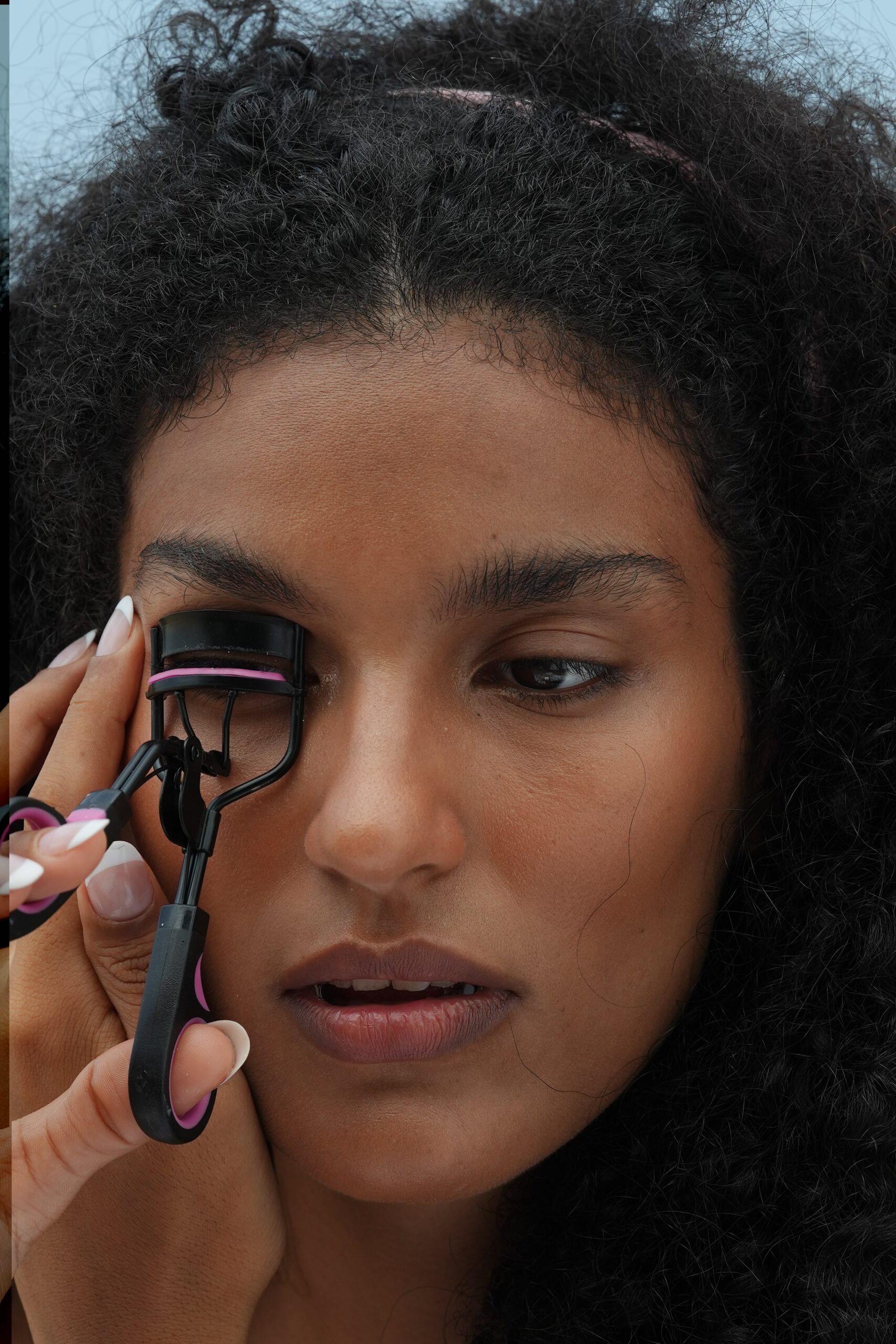 A person uses an eyelash curler, demonstrating a simple step for a quick and easy, office-ready makeup look.