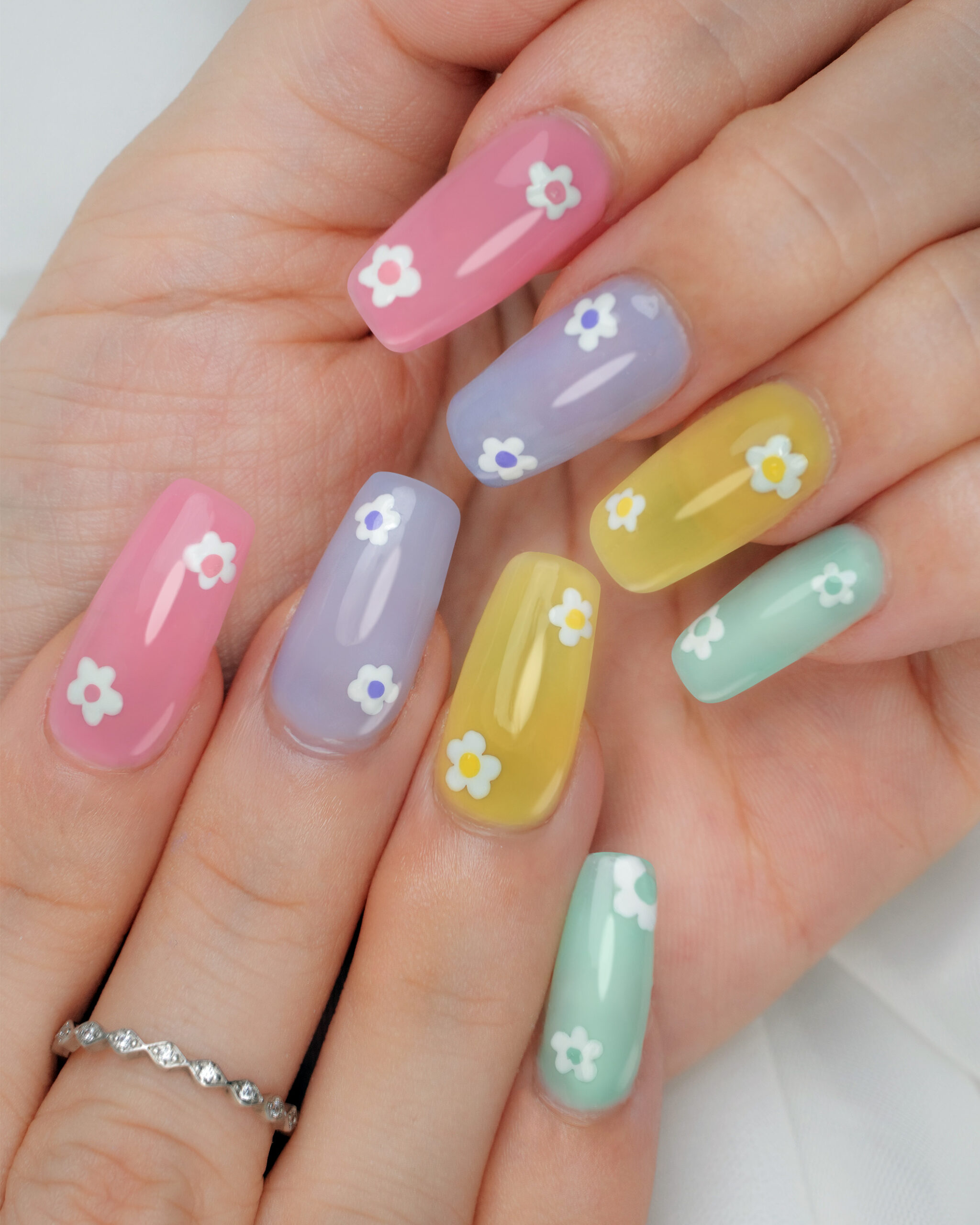 A close-up of hands with trendy gel nails featuring a pastel, flower-inspired design, showcasing a cute and modern manicure trend for 2025
