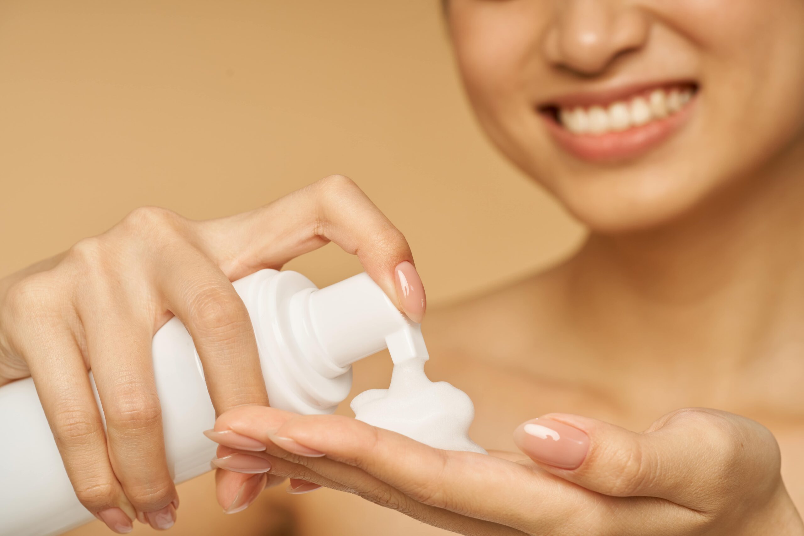 A person smiles while dispensing a white foam cleanser into their hand, showcasing a gentle and effective formula for the best skincare choice.
