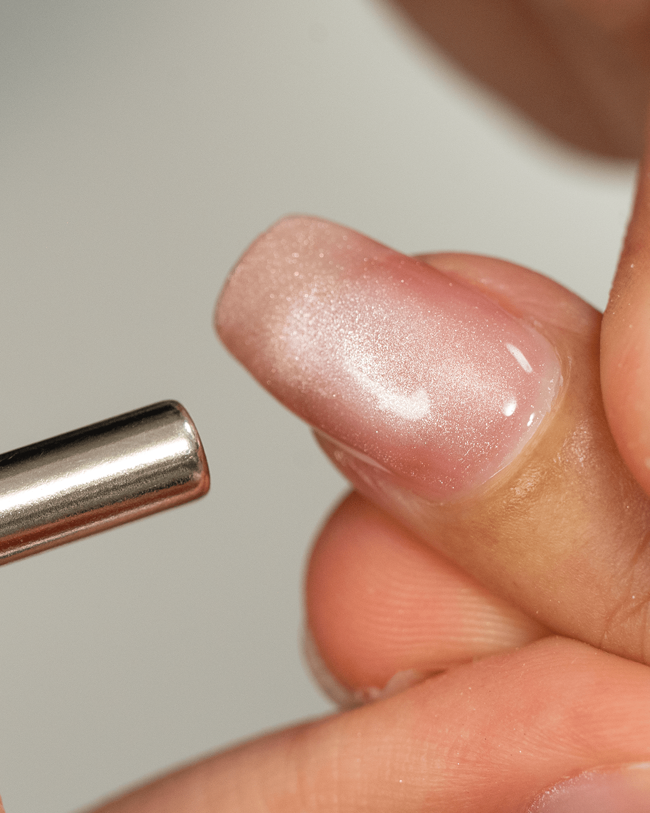 A close-up of a person's hand using a magnetic tool to create a cat eye effect on a translucent gel nail, demonstrating a key step in a magnetic manicure tutorial.