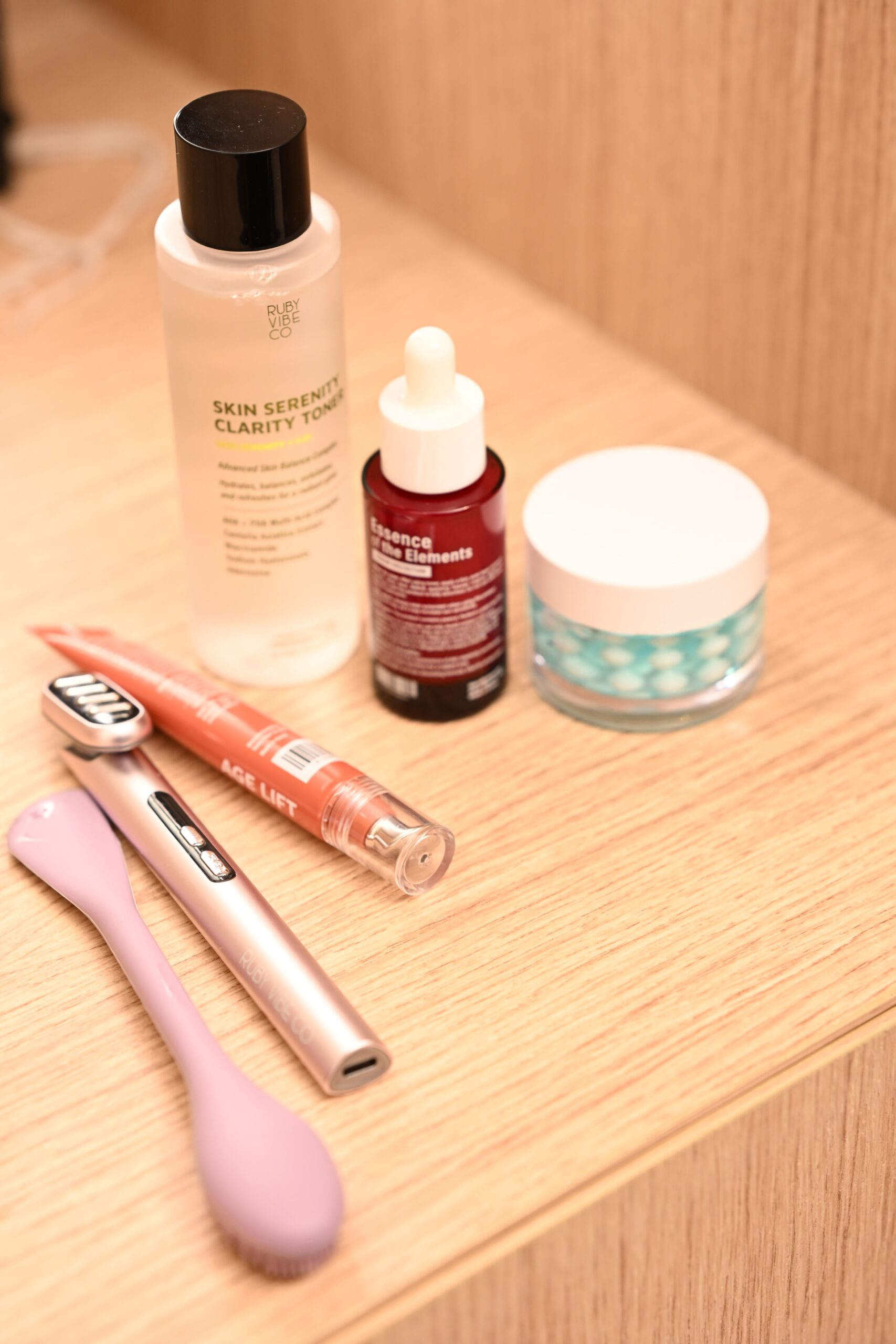A collection of skincare products, including toner, serum, and facial tools, laid out for a dewy skin makeup tutorial.