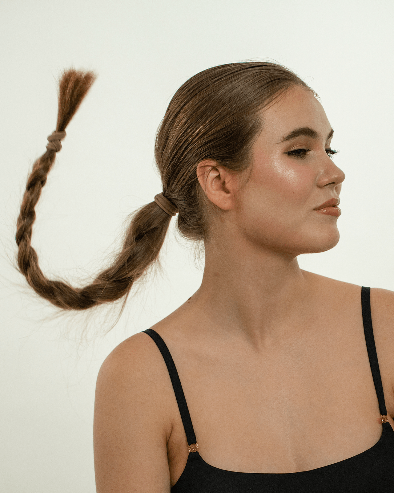A side profile of a woman with a braid, showcasing her finished makeup look with a very noticeable dewy and radiant skin finish.