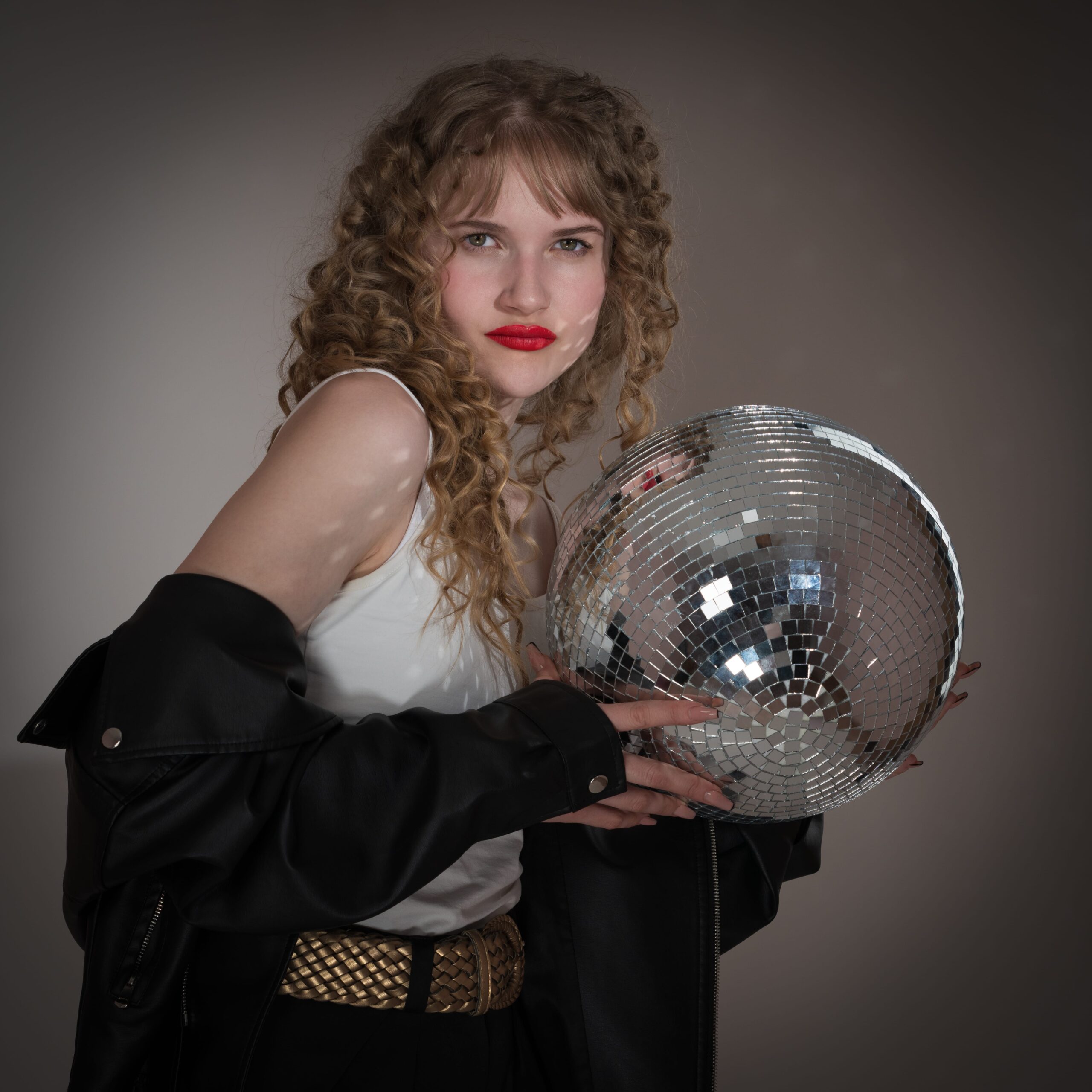 A woman with curly hair and a bold red lip holds a disco ball, a fun and vibrant style inspired by Taylor Swift's iconic look.