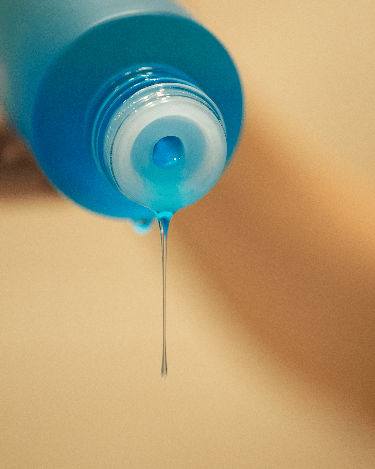 A close-up shot of a blue liquid dripping from a bottle, highlighting the light and fluid texture of the makeup remover.