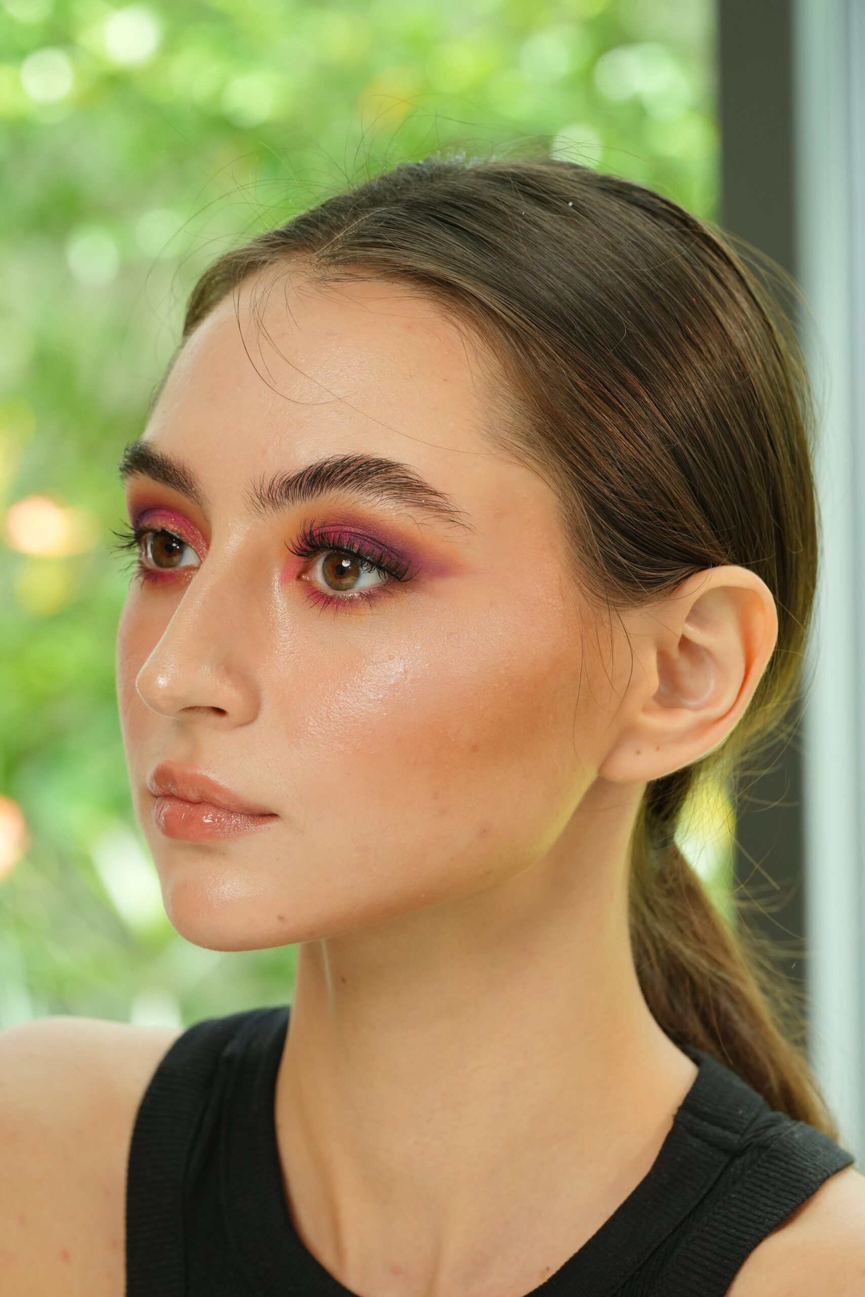 A side portrait of a woman with a light-to-medium skin tone wearing glossy nude lipstick and bold eye makeup, a visual example for a guide on finding the perfect nude shade.