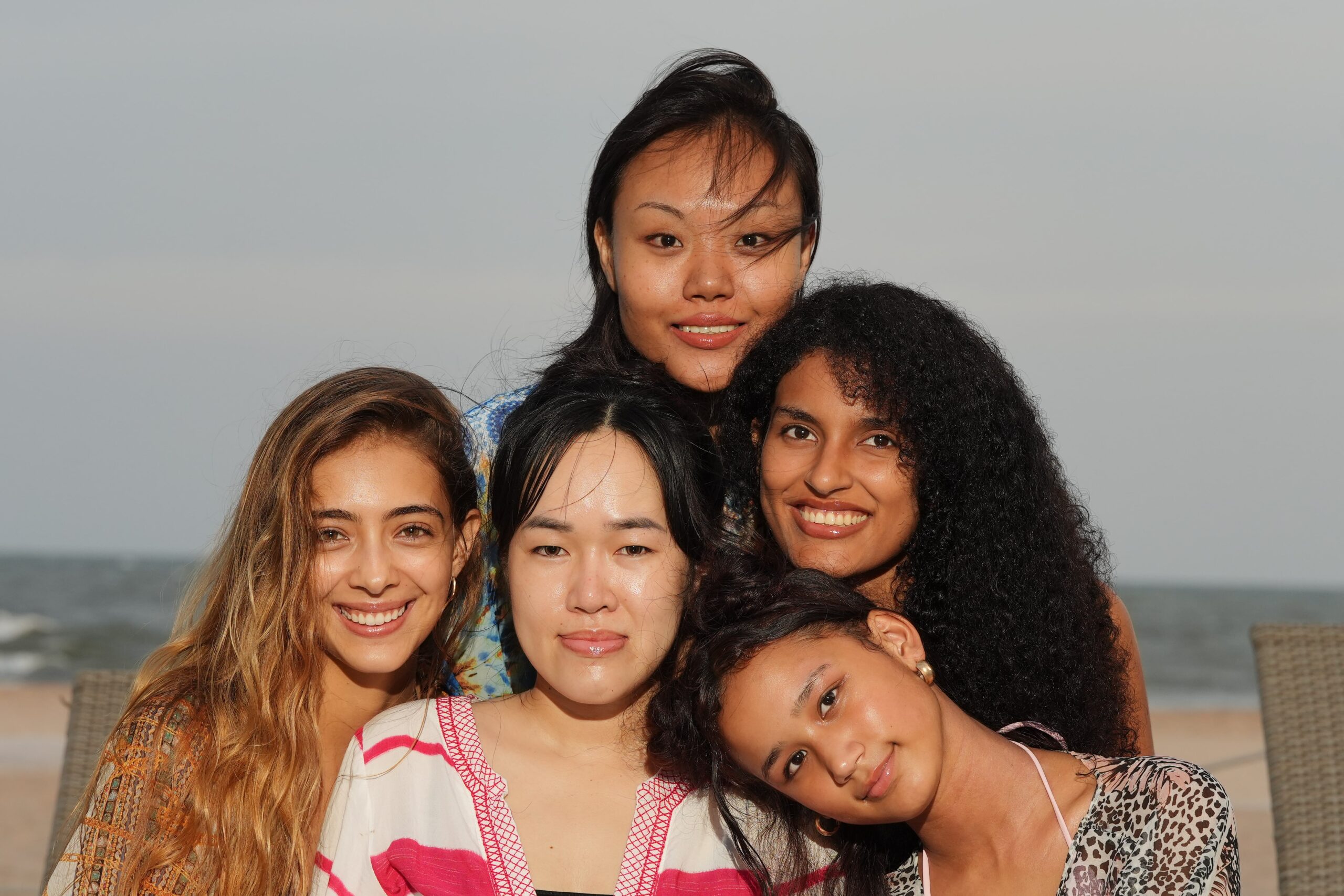 A group of diverse women smiling on a beach, representing a guide to finding the perfect red lipstick for every skin tone.