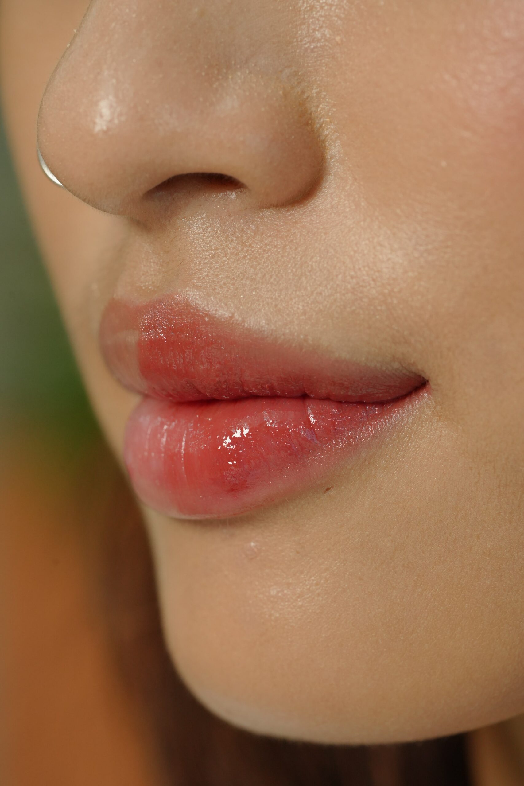 A close-up of a person's lips with a glossy light red lipstick, showing a shade that complements a specific skin tone.