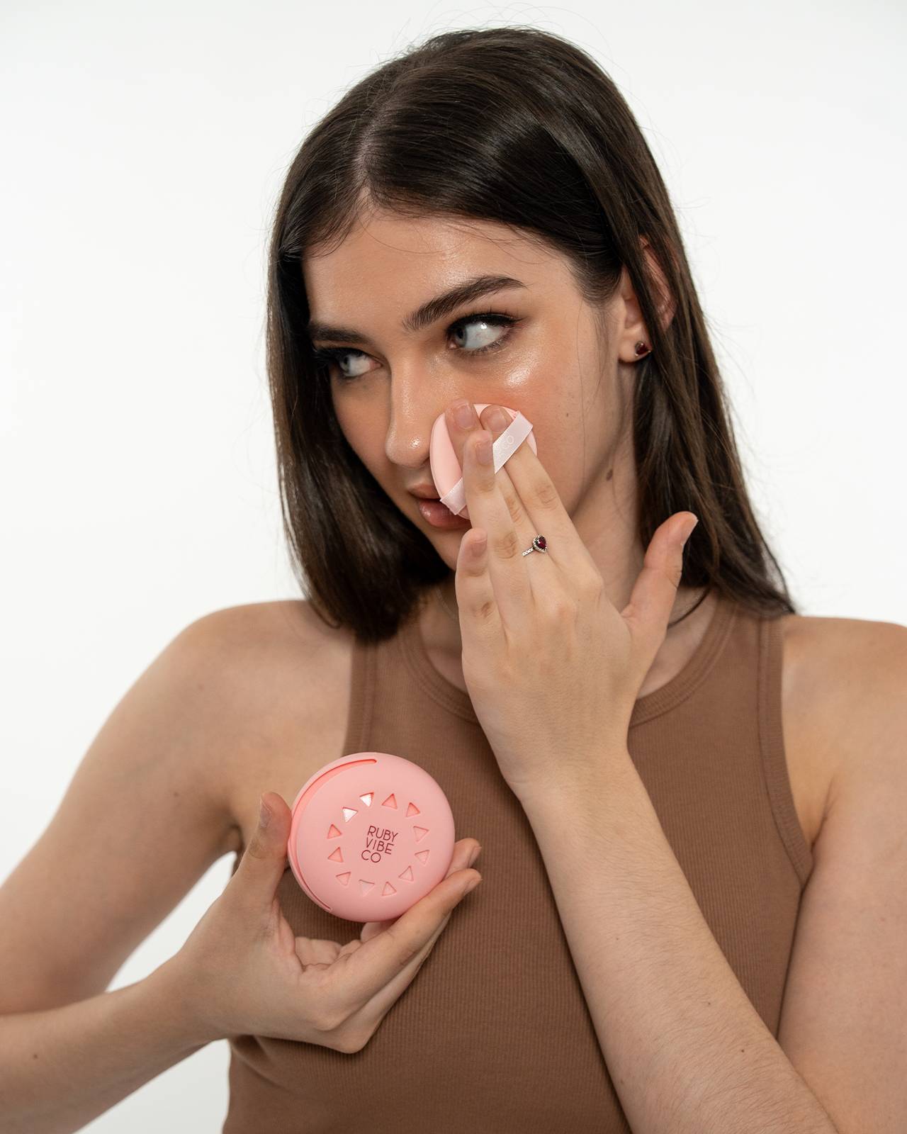 A woman sets her makeup with a pressed powder compact from 'Ruby Vibe Co,' a key step for a perfect, long-lasting nude lipstick finish.