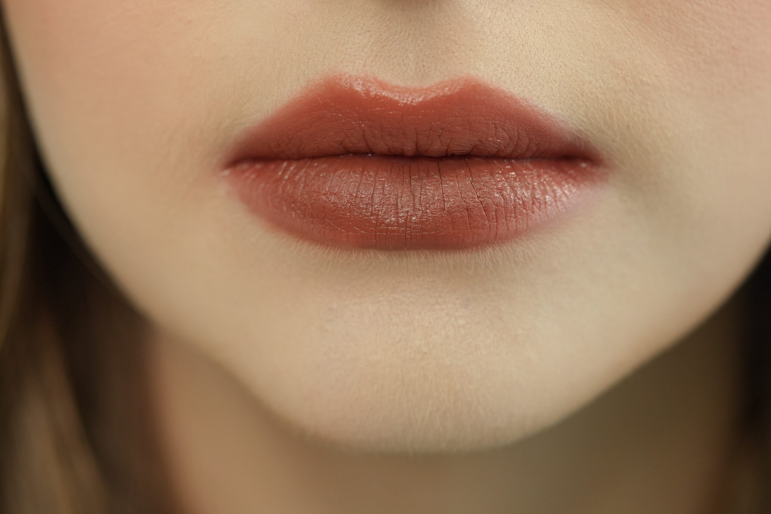 A close-up of a person's lips with a subtle nude or light brown lipstick, showcasing a perfect finish.