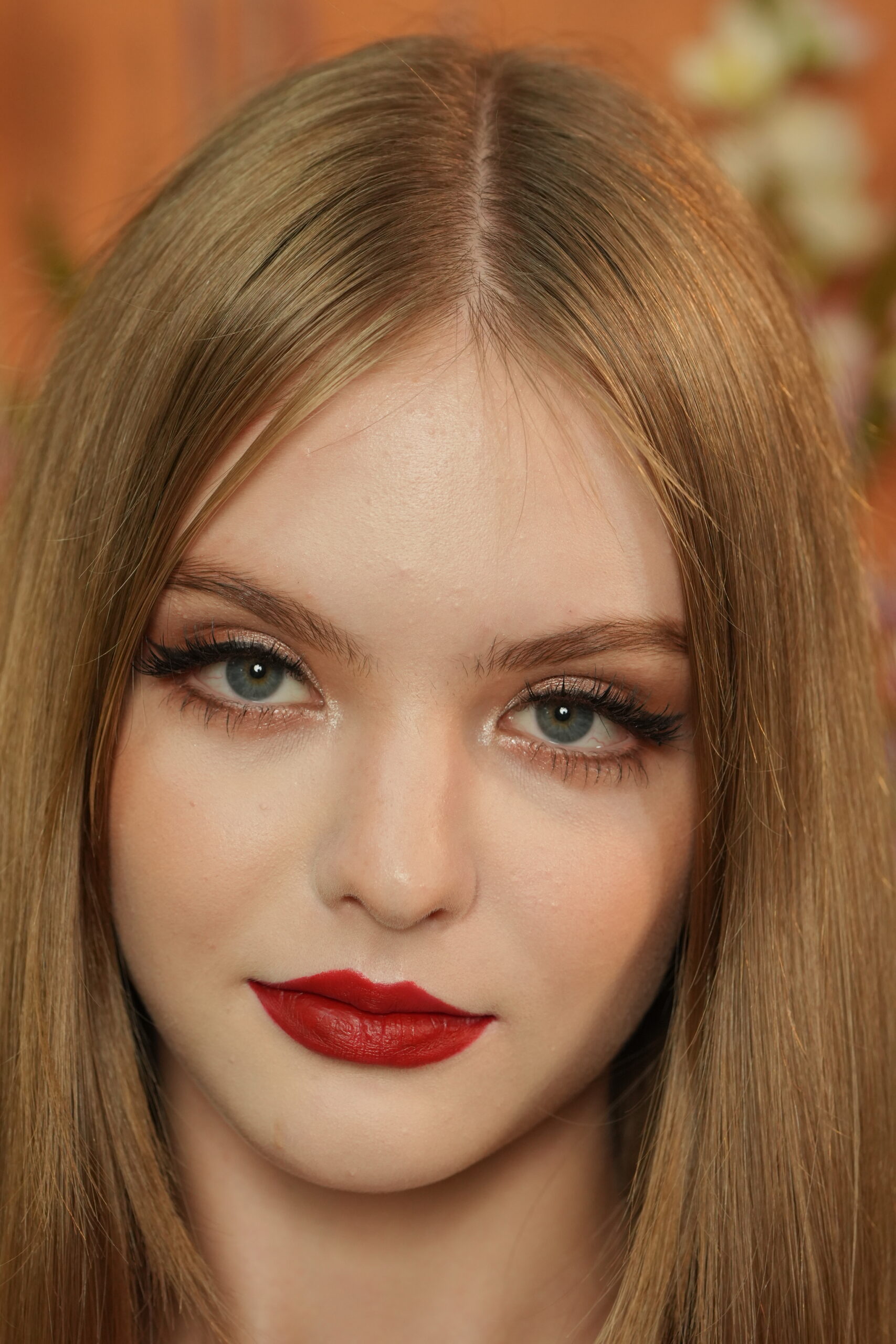 A close-up of a woman with a vibrant, glossy red lip, holding her finger to her mouth in a 'shushing' gesture, showcasing a flawless finish inspired by Taylor Swift.