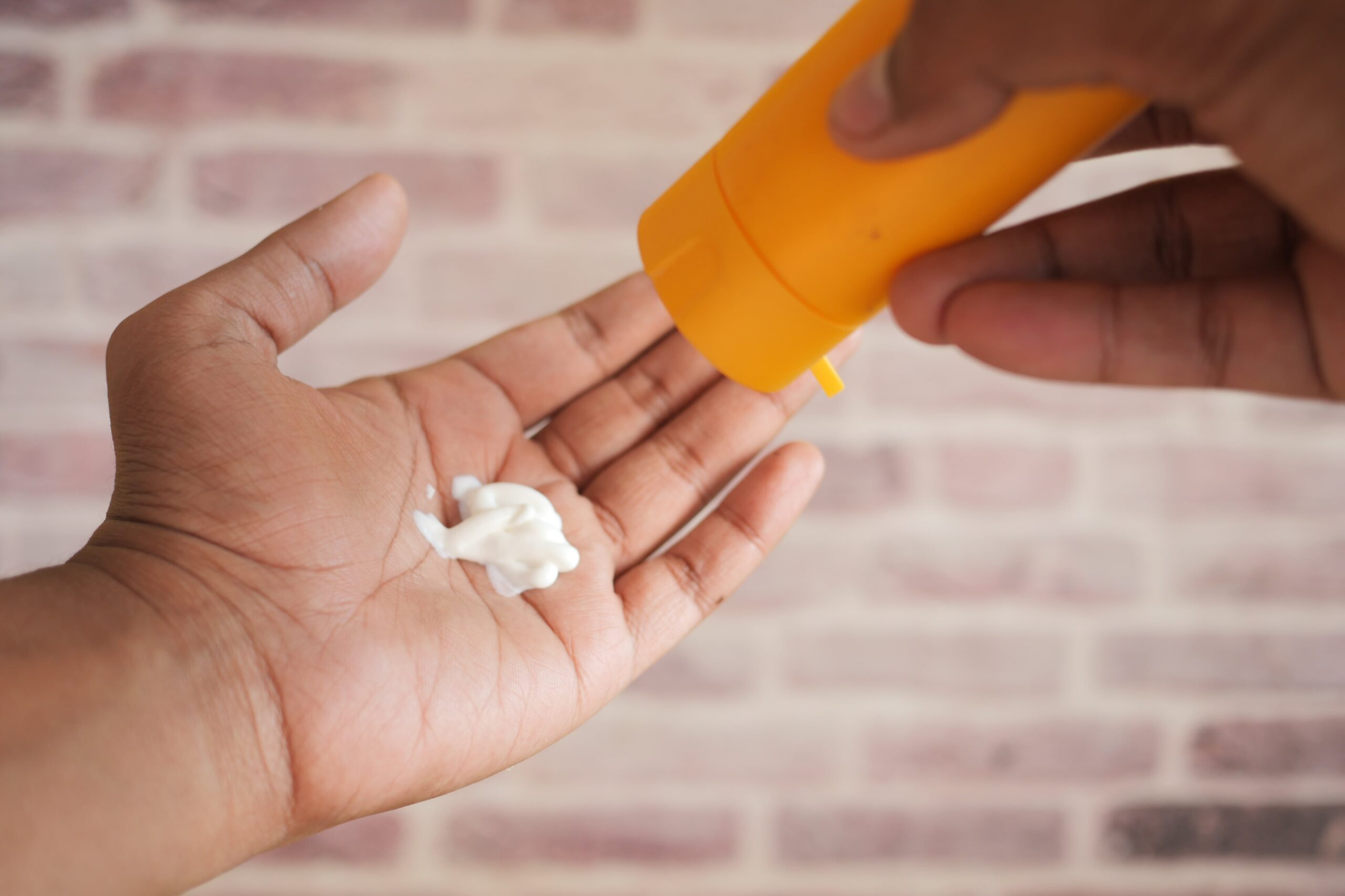 A person's hand applies a cream from a yellow tube into their hand, showing a practical application step for a retinol routine