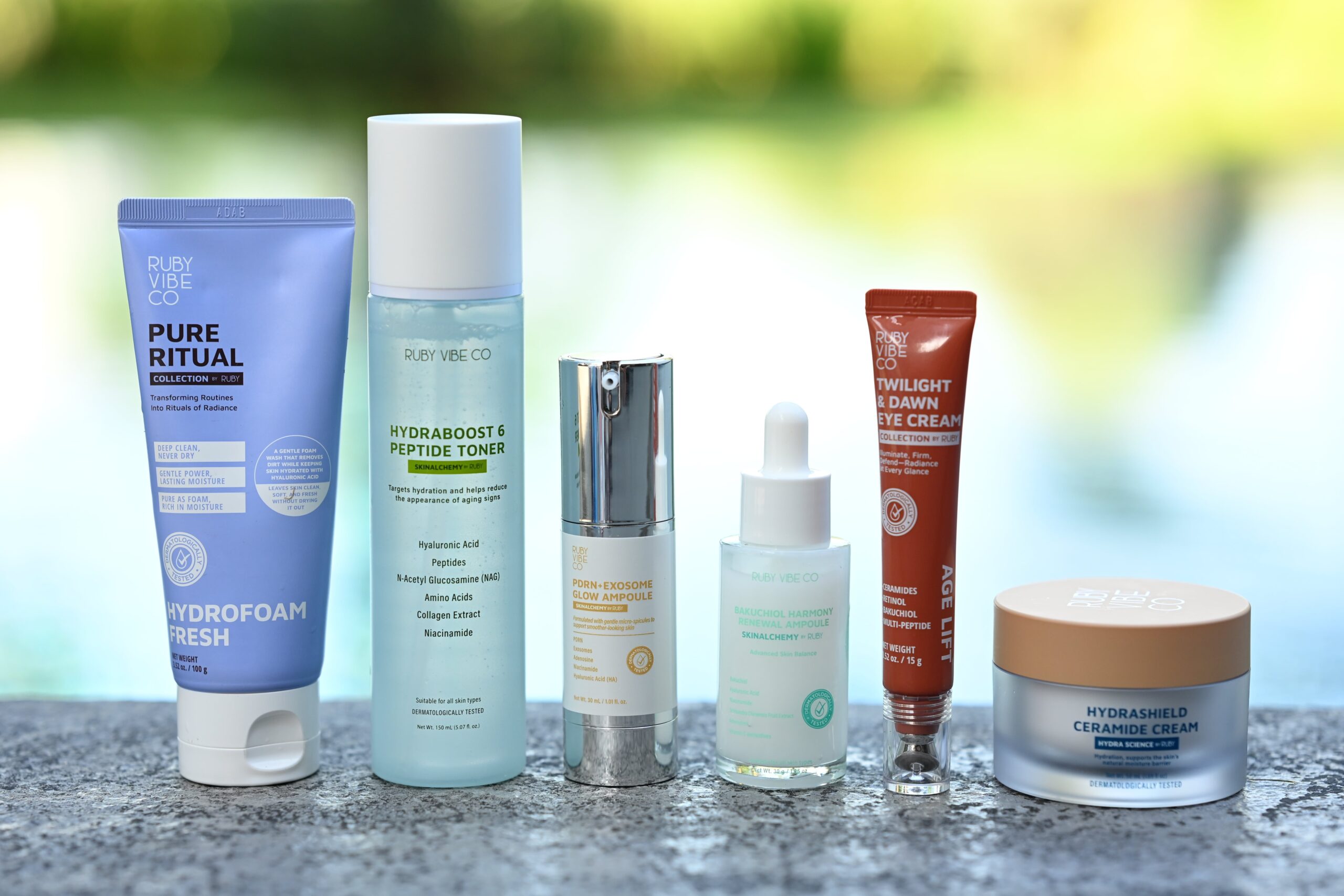 An assortment of skincare products from the brand Ruby Vibe Co. The products include a Hydrofoam Fresh cleanser, Hydraboost & Peptide Toner, a serum, a Twilight & Dawn Eye Cream, and a Hydrashield Ceramide Cream. This image visually represents a complete skincare routine.