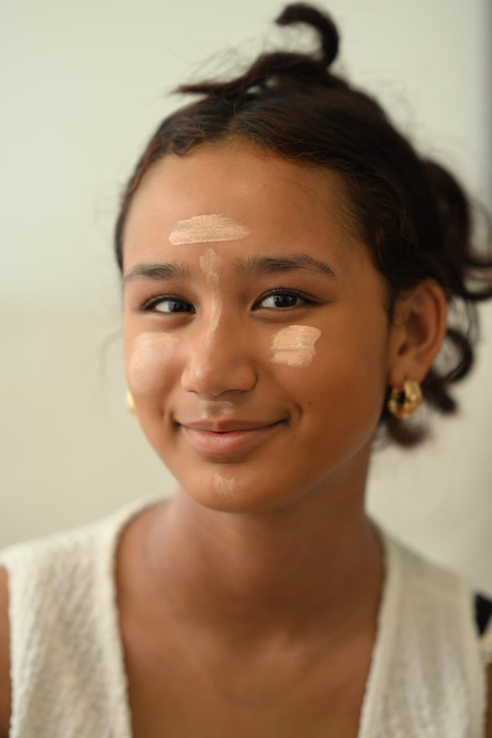 A person with stripes of foundation on their face smiles, ready for the blending step in a beginner's tutorial for a natural, glowing look.