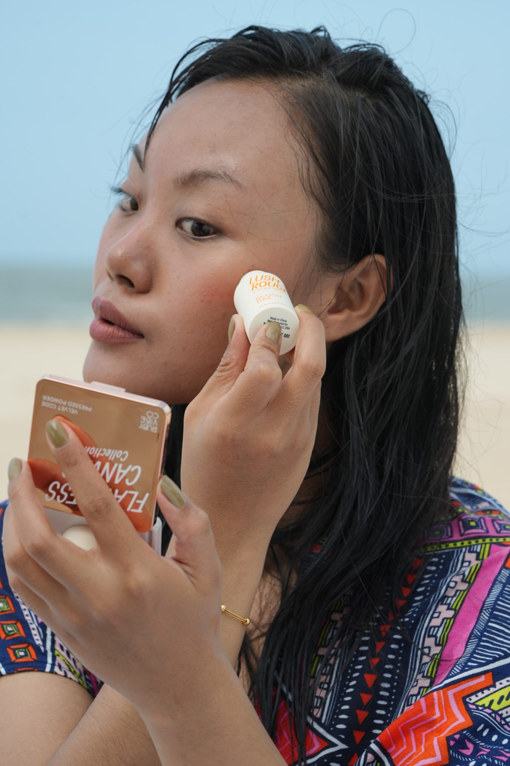 A person applies a stick blush to their cheek while holding a mirror, a simple and quick technique for a natural glow.