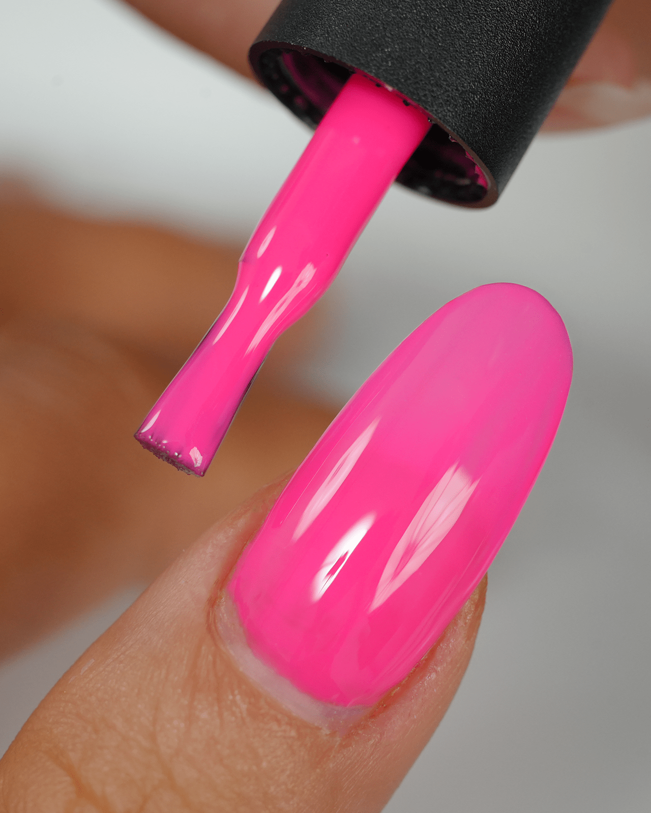A close-up of a nail being painted with a hot pink gel polish. The image focuses on the glossy finish and vibrant neon color, perfect for a bright summer manicure.