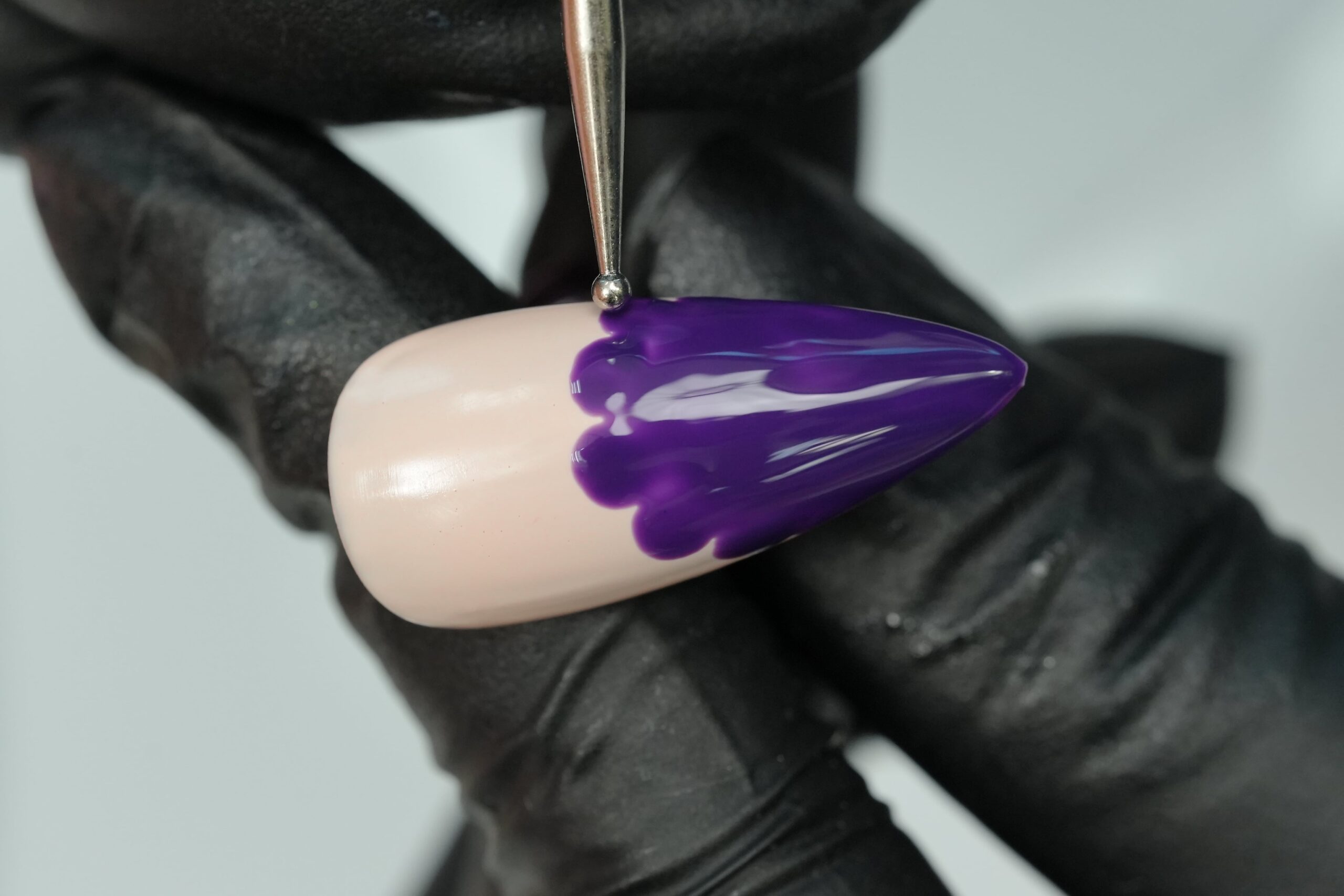  A close-up shot of a person wearing black gloves, using a nail art brush to create a purple design on a false nail. This image highlights the process of intricate nail art with bold, bright colors.