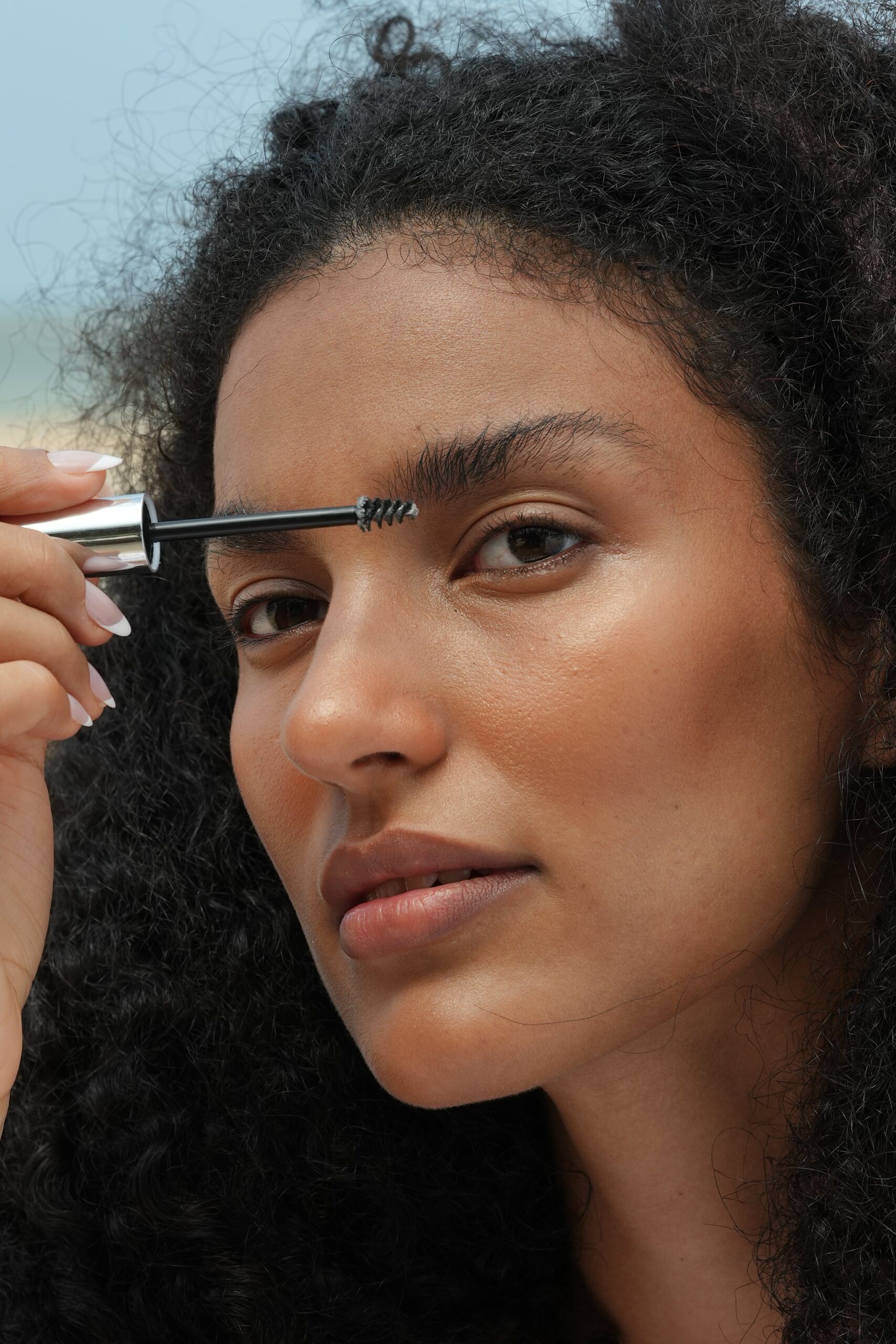 A close-up of a person defining their eyebrows with a spoolie brush, a simple step in a 'no-makeup' tutorial for a polished but natural look.