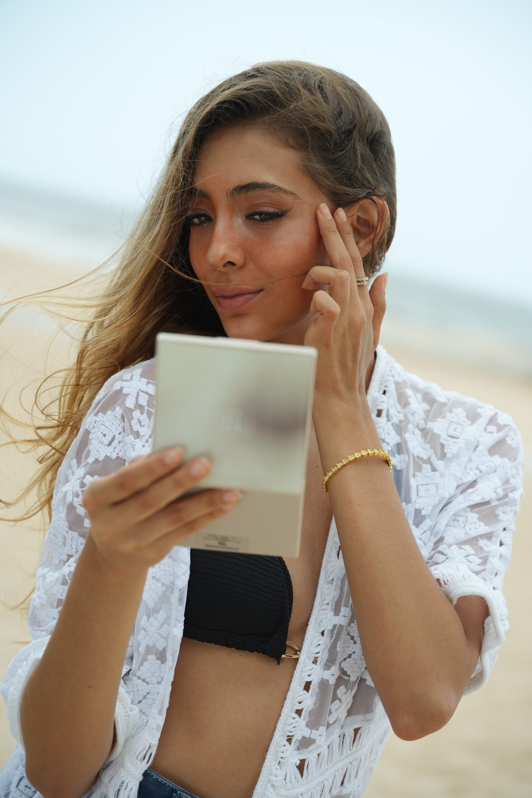 A woman looks into a compact mirror while gently touching her face, demonstrating a step in a quick and easy 'barely-there' makeup tutorial.