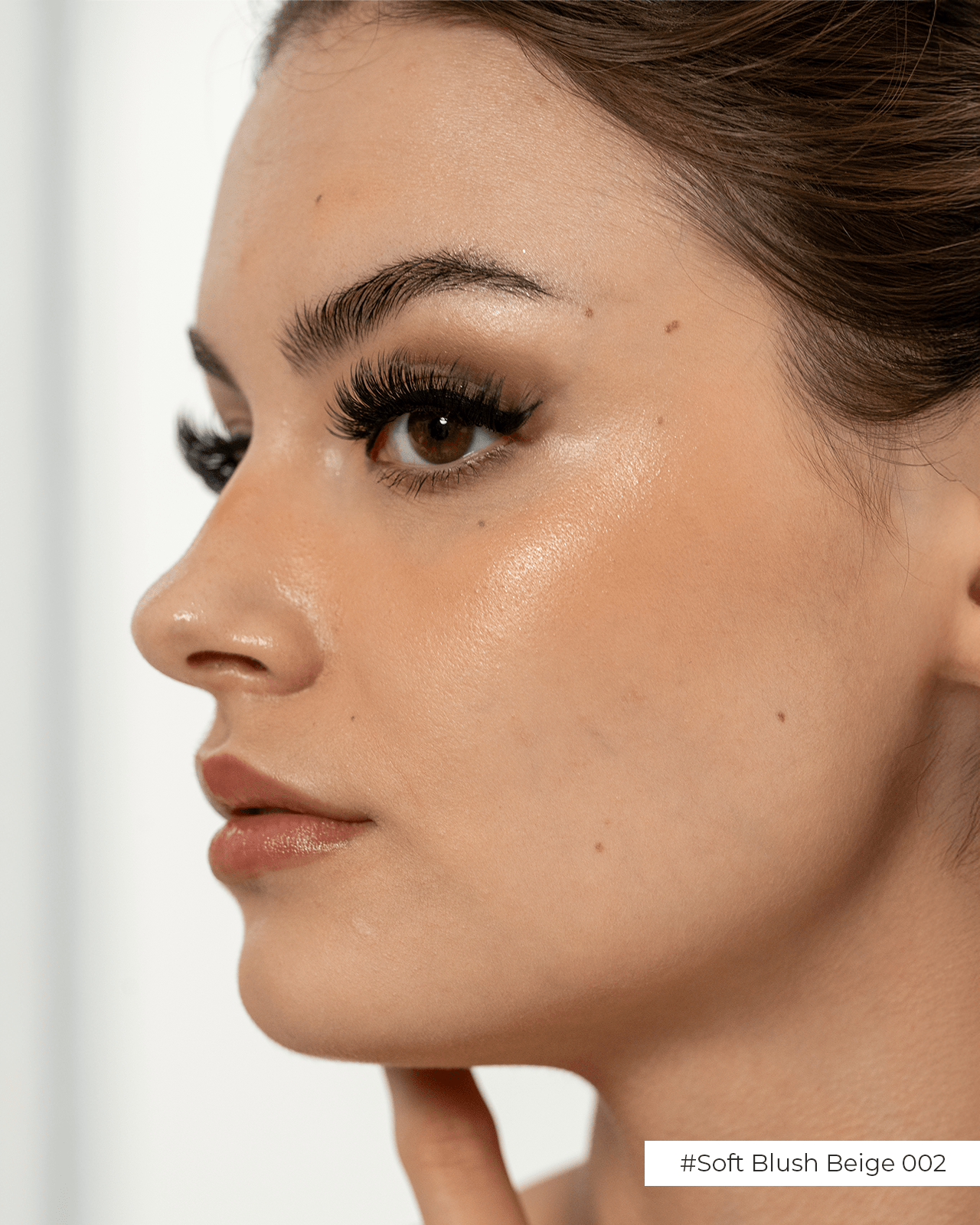A close-up side profile of a woman with a glossy nude lip and a glowing complexion, showing a finished, cohesive makeup look.