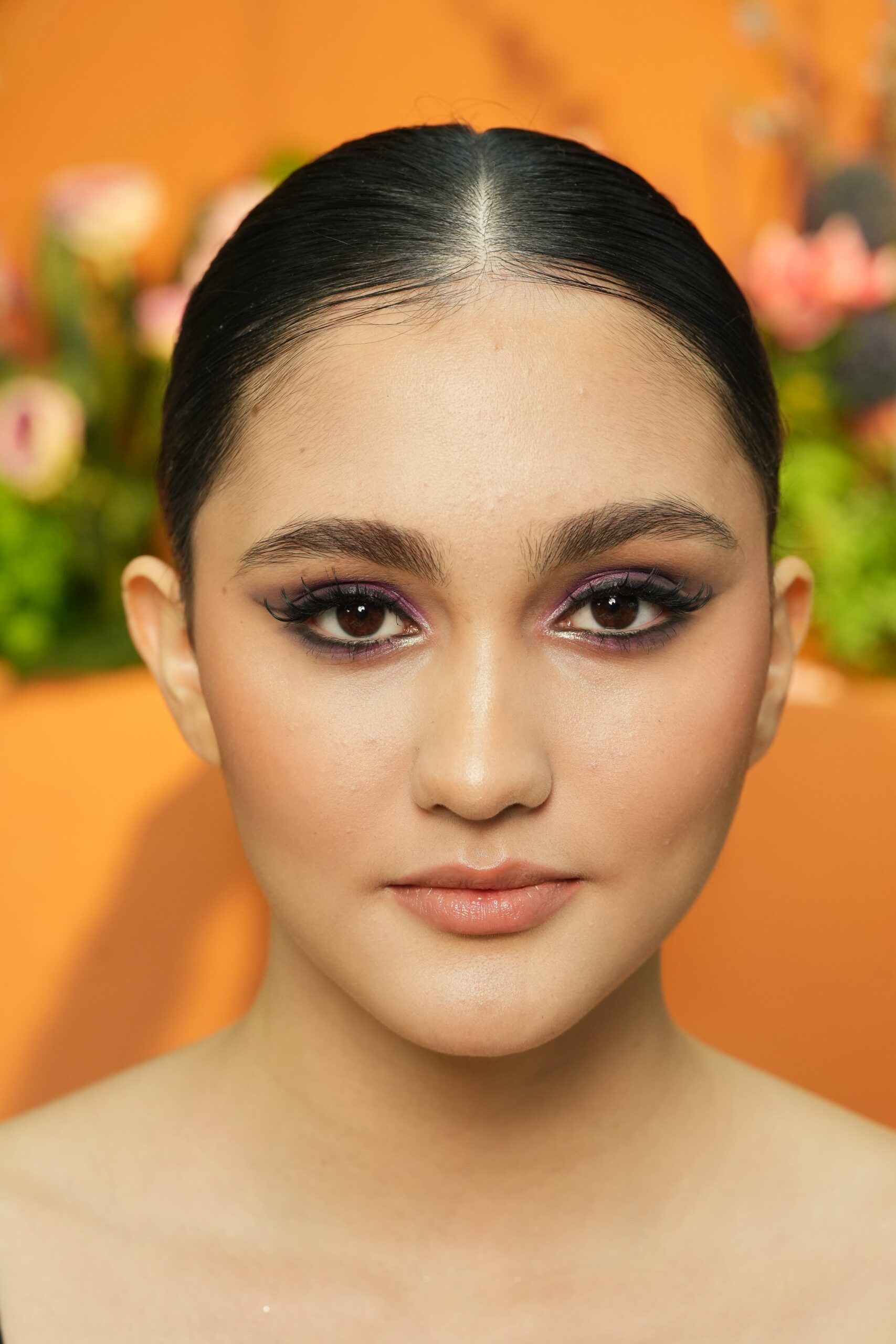 A woman with a sleek updo and bold purple eyeshadow, demonstrating a sophisticated look where a nude lipstick provides a perfect balance for an evening event.