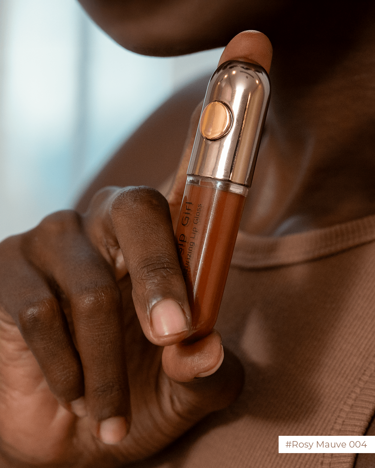 A person holds a 'Rosy Mauve' nude lip gloss, a product for achieving a glossy finish.