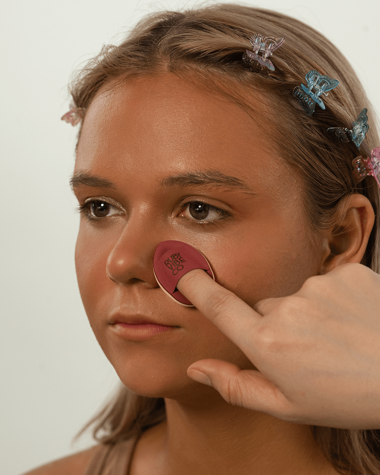 A person applies a mattifying product to a woman's nose with a sponge, a targeted technique for a smooth, fresh makeup finish for oily skin.