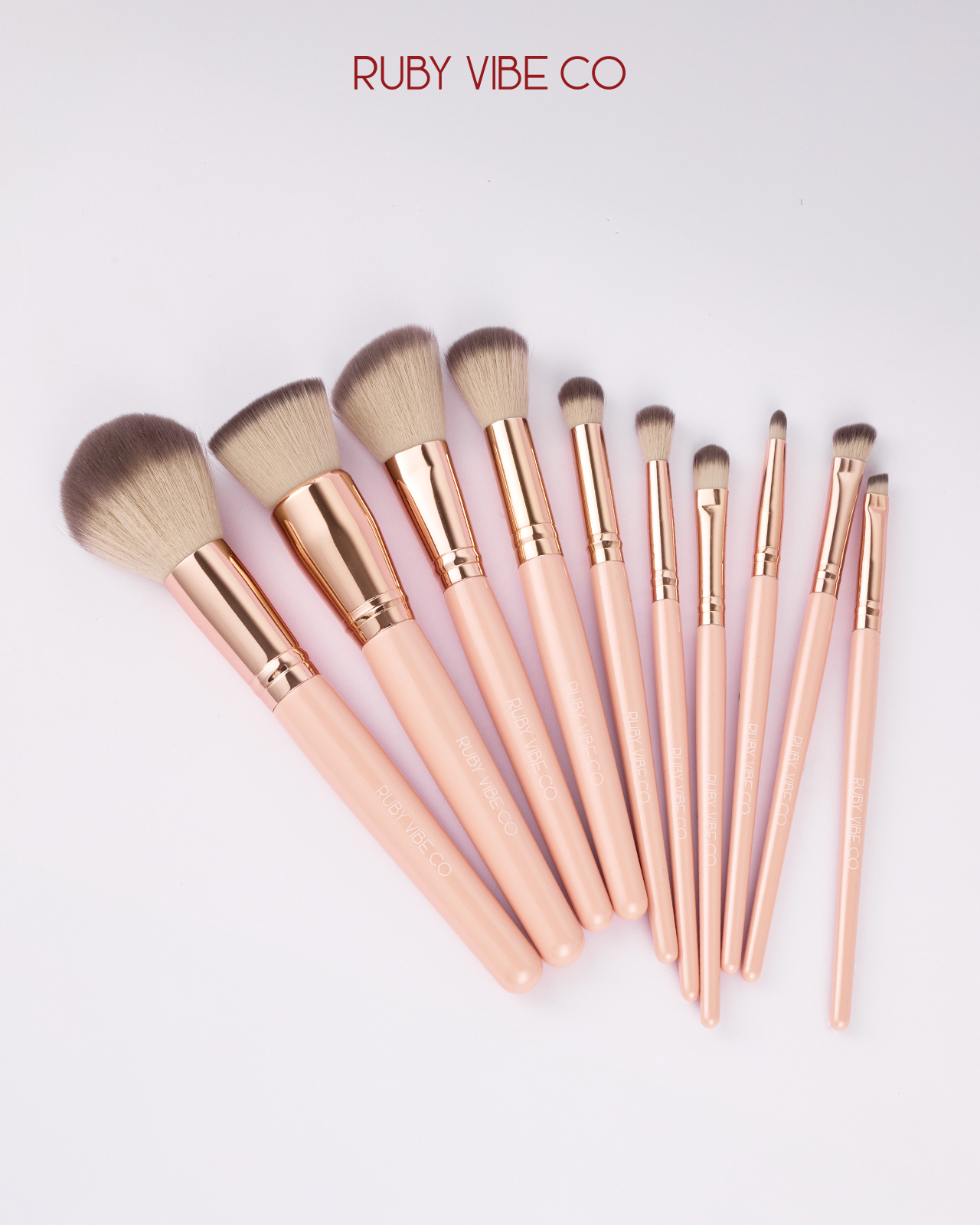 A professional set of 'Ruby Vibe Co' makeup brushes with light pink handles, showcasing a variety of shapes and sizes for a full artist's kit.