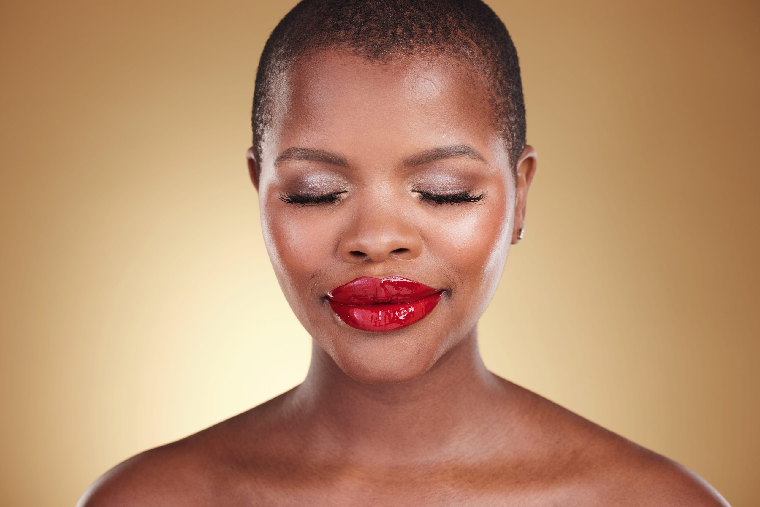 A close-up of a person's face with a bold, glossy red lipstick. Their eyes are closed, showing a serene expression, which highlights the confidence and striking effect of a flawless red lip application.