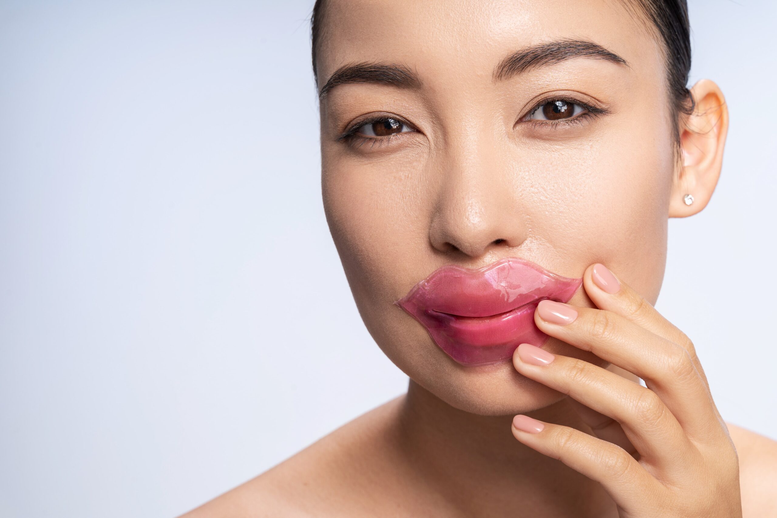 A woman with a lip mask on, gently touching it with her hand. The image showcases the use of lip masks as an intense hydration treatment for a plump, healthy, and flawless base.