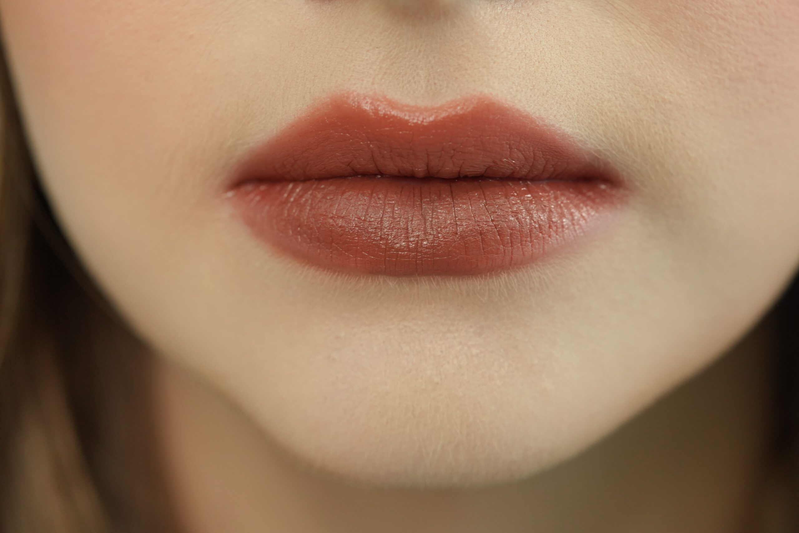 A close-up of a person's lips with a matte, rusty brown lipstick. The texture of the lips is visible, emphasizing the importance of a smooth surface for a clean and even finish, especially with matte formulas.