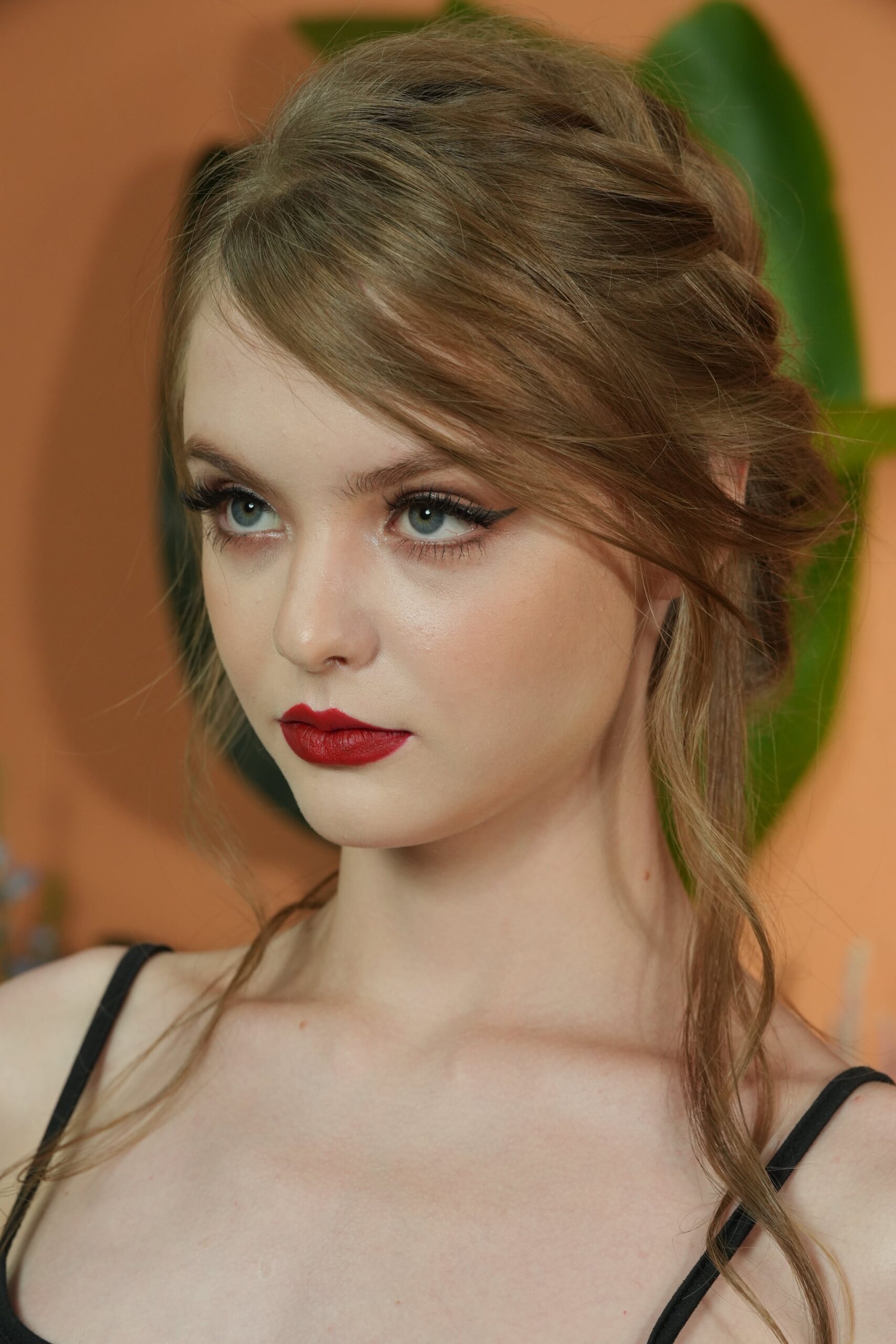 A close-up portrait of a woman with long, light-brown hair and blue eyes, confidently wearing classic red lipstick. The makeup is bold and defined, emphasizing the power and versatility of a classic red lip