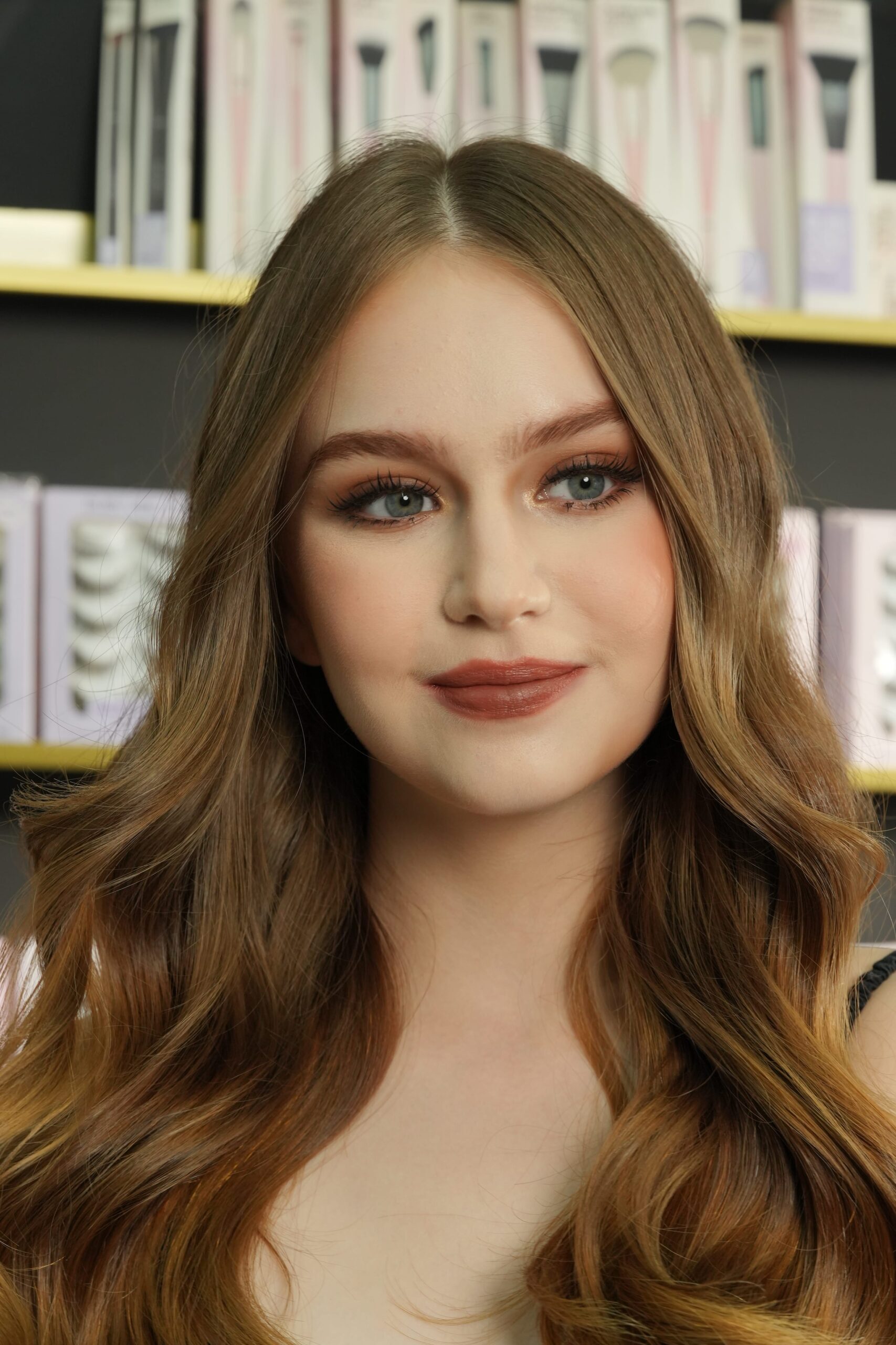 A portrait of a woman with long, wavy brown hair, wearing a more subtle, terracotta-red lipstick. She is smiling gently, showing a more natural, everyday way to wear a red lip. This photo provides an example of a less intense red shade for different occasions.