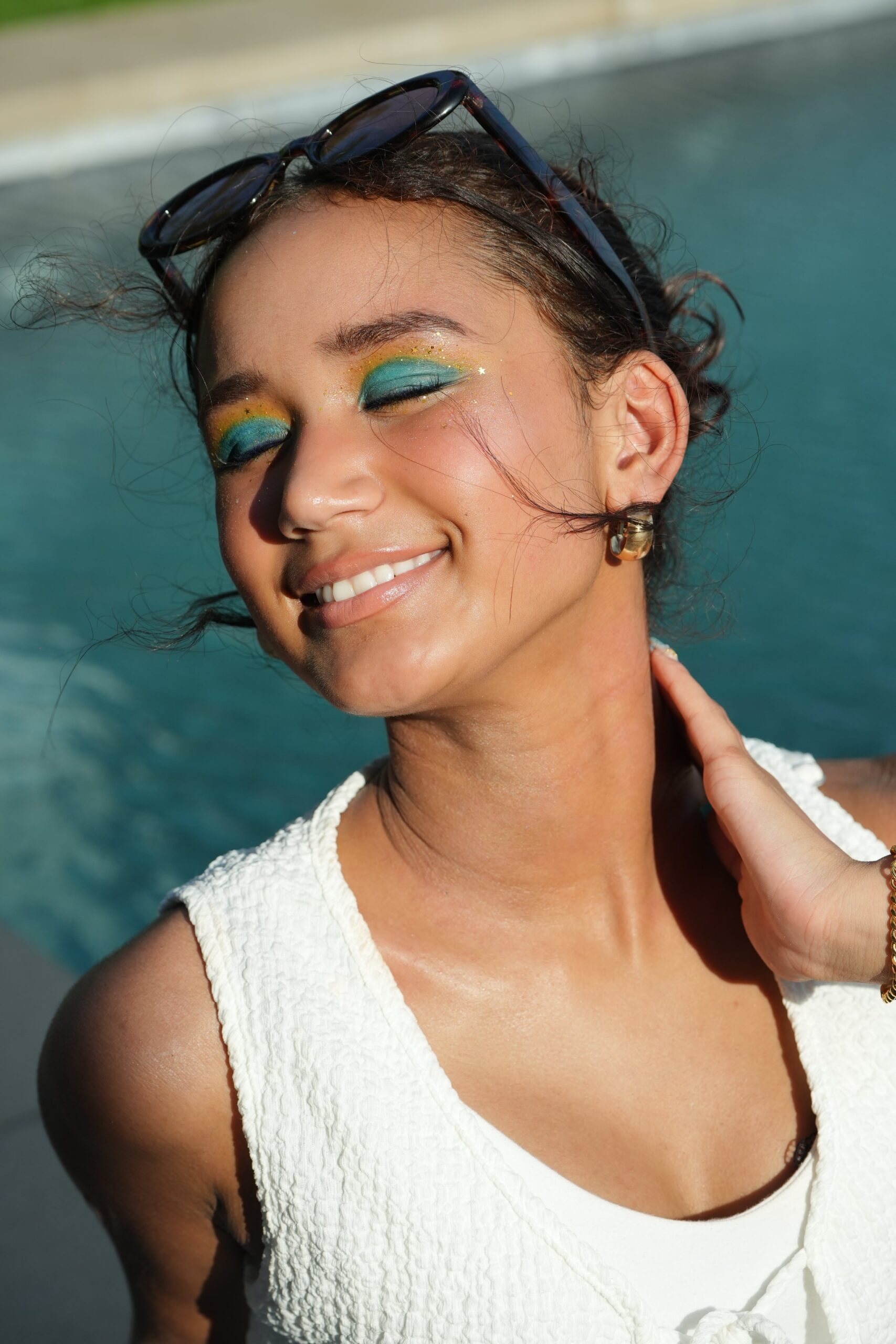 A woman smiles, showcasing a final makeup look with colorful eyeshadow and glitter, perfect for a beginner's tutorial.