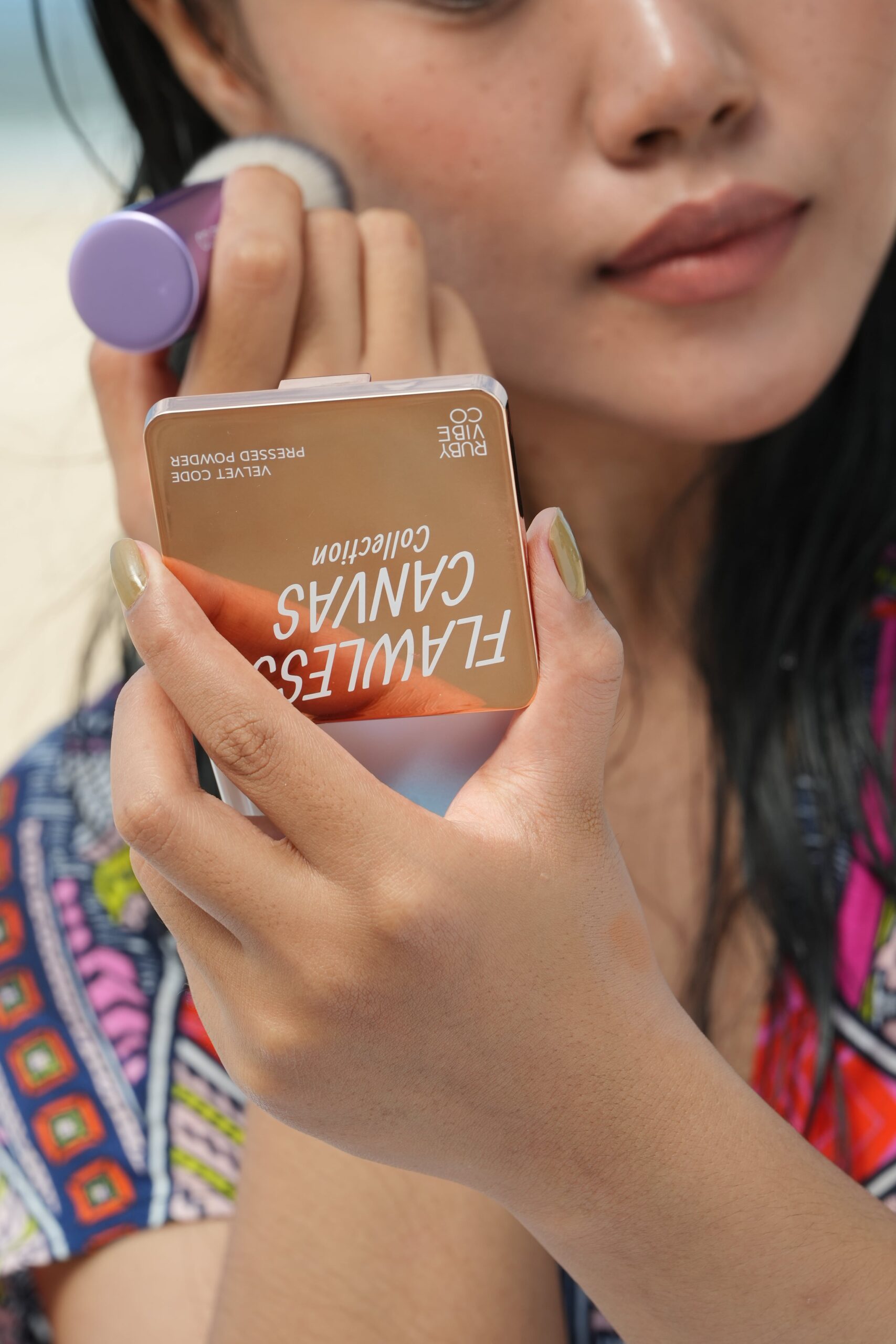 A close-up of a hand holding a 'Ruby Vibe Co Flawless Canvas Pressed Powder' compact and brush, demonstrating a step in a beginner's makeup routine.