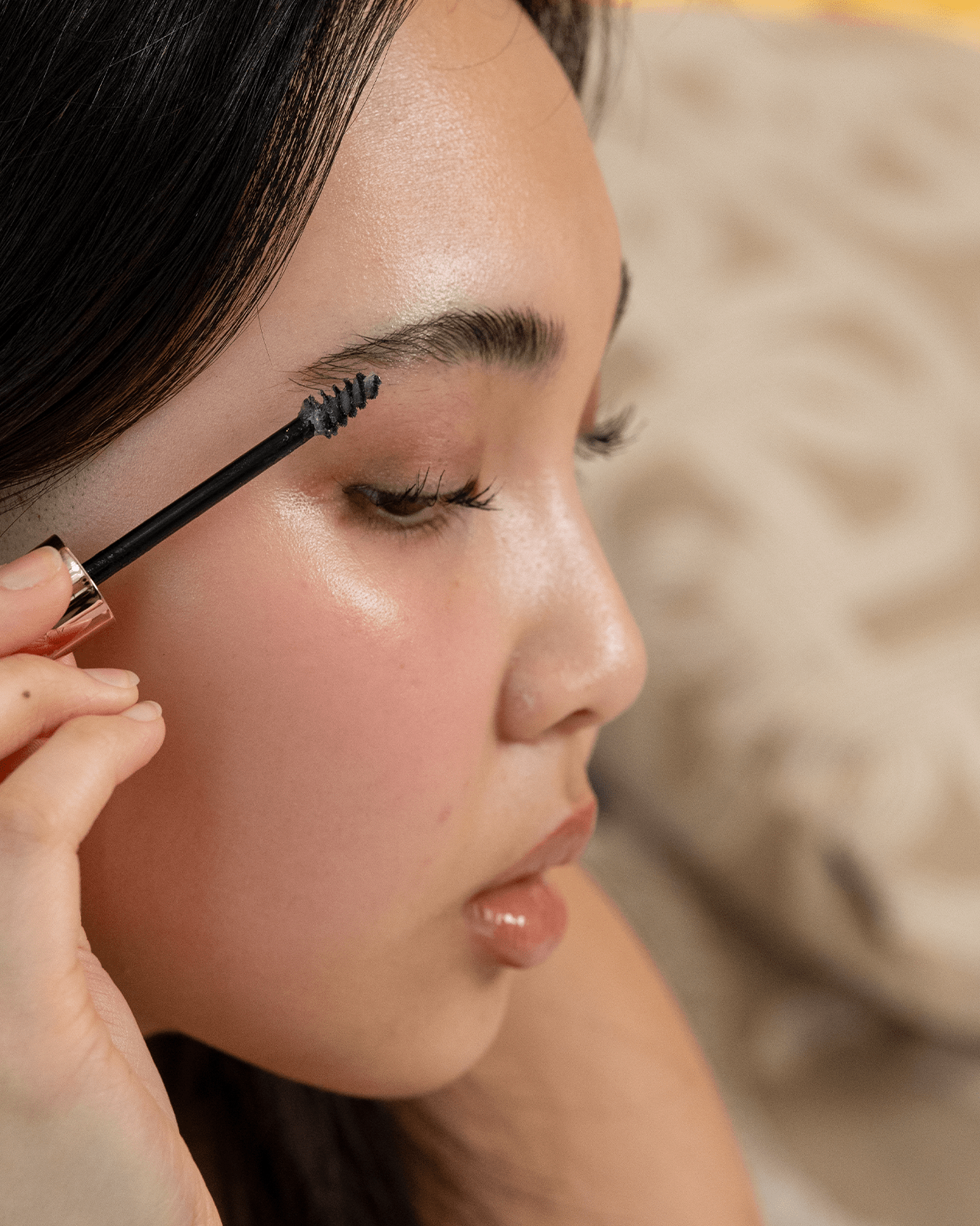 A side-profile shot of a young person applying eyebrow gel with a spoolie brush, demonstrating a gentle and natural approach to makeup.