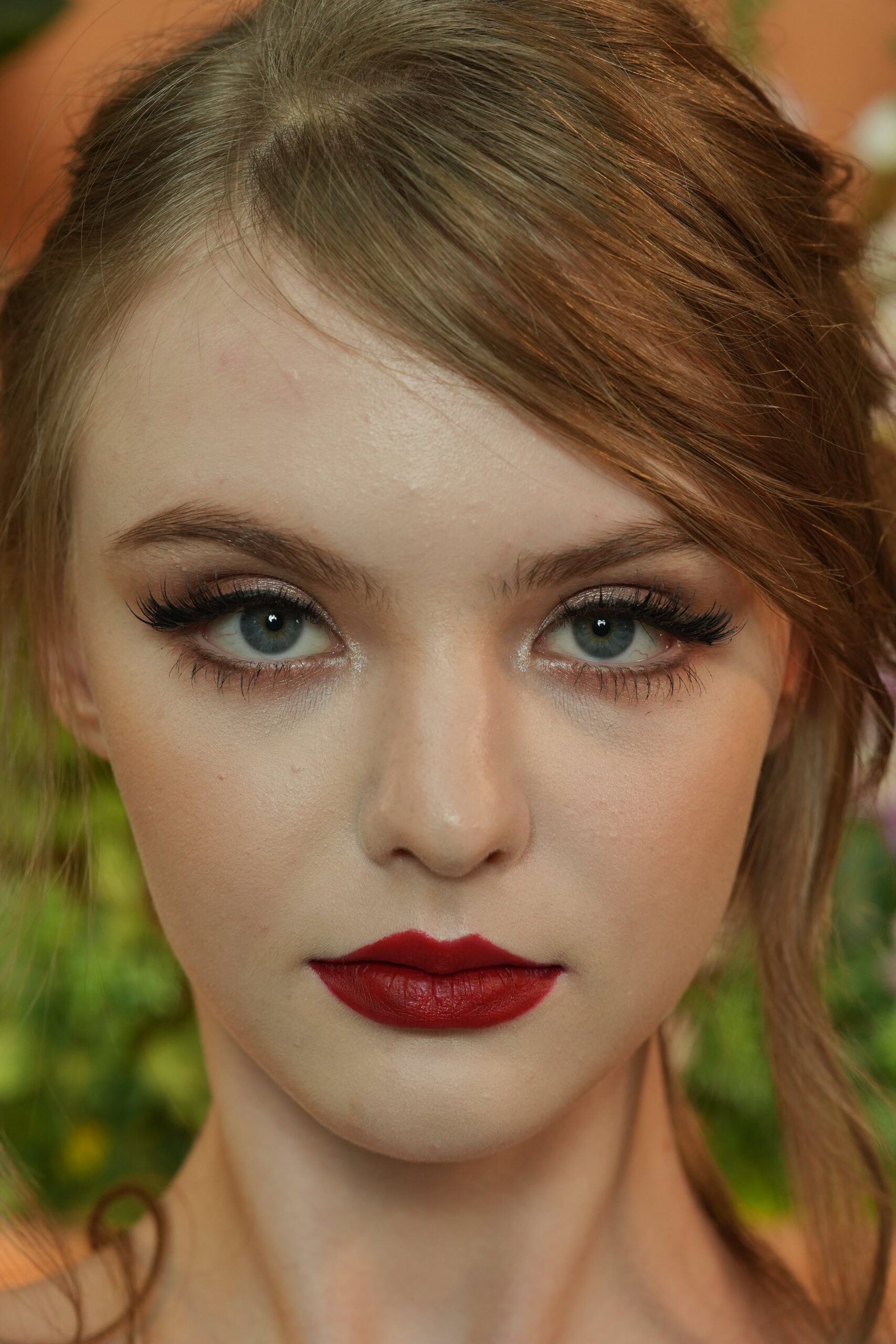 close-up, straight-on portrait of a woman with light brown hair and blue eyes, wearing a bold, classic matte red lipstick. The image focuses on her serious, direct gaze, emphasizing the confidence and power that a red lip represents.