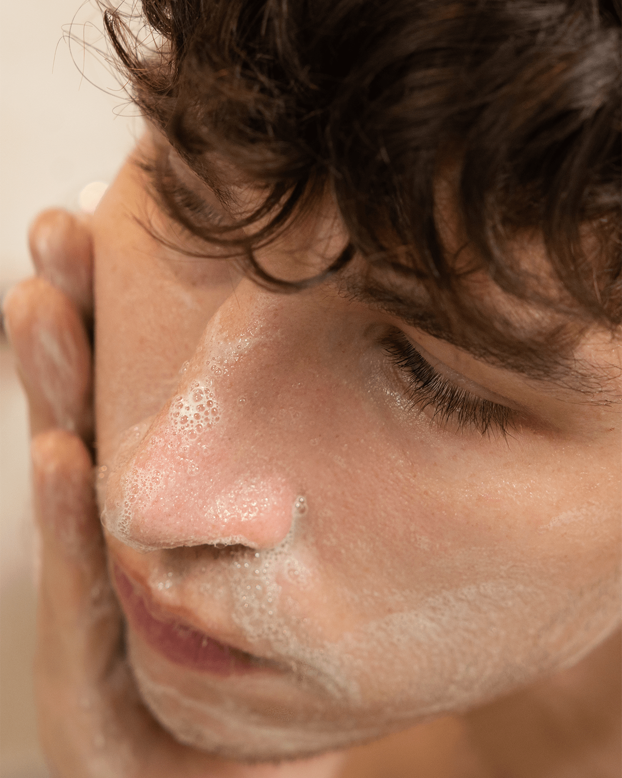 A close-up shot of a person washing their face with a gentle, foaming cleanser, demonstrating the most important step in a skincare routine.