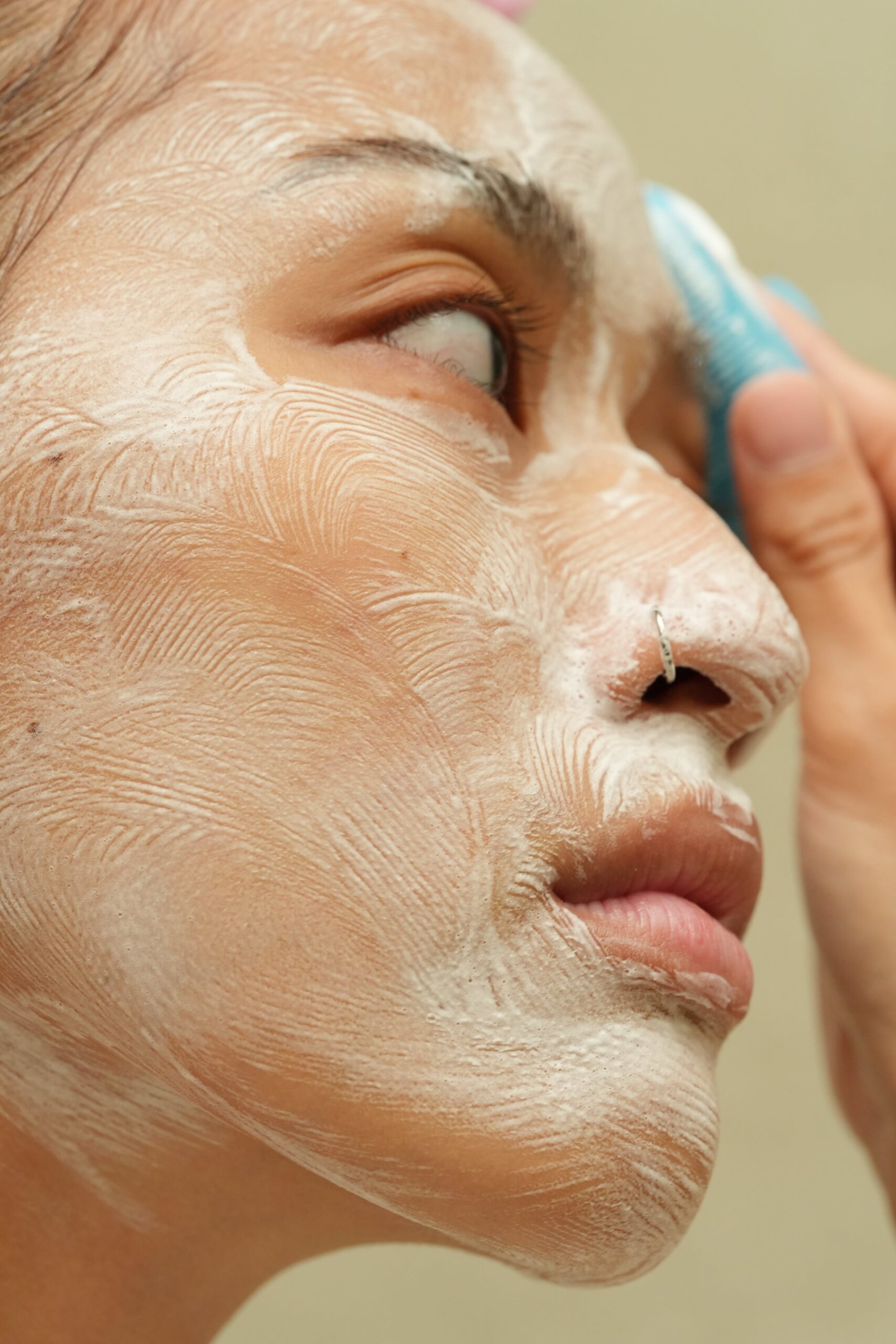 A close-up of a person's face being cleansed with a blue facial brush and foaming cleanser, showing a technique for deep cleansing based on skin type.