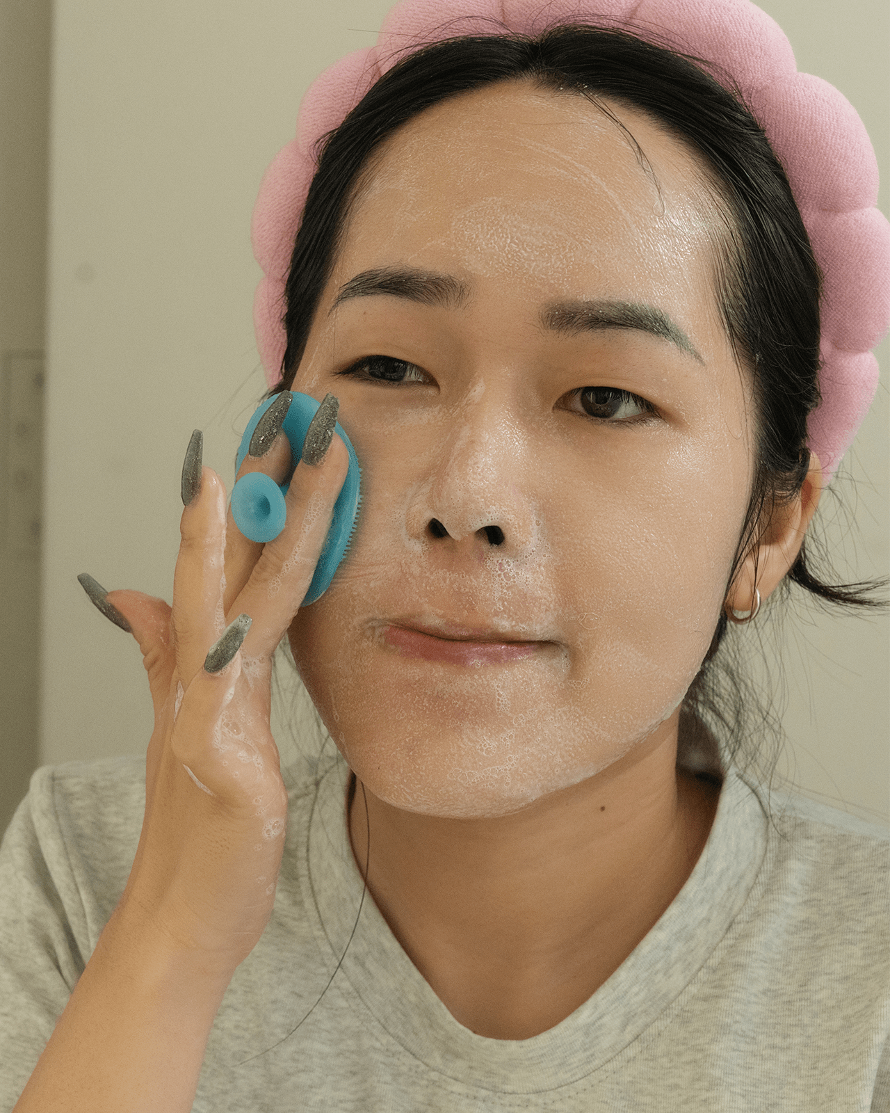 A woman with a pink headband applies a clay mask, showing a perfect use case for a skincare headband to keep hair clean.