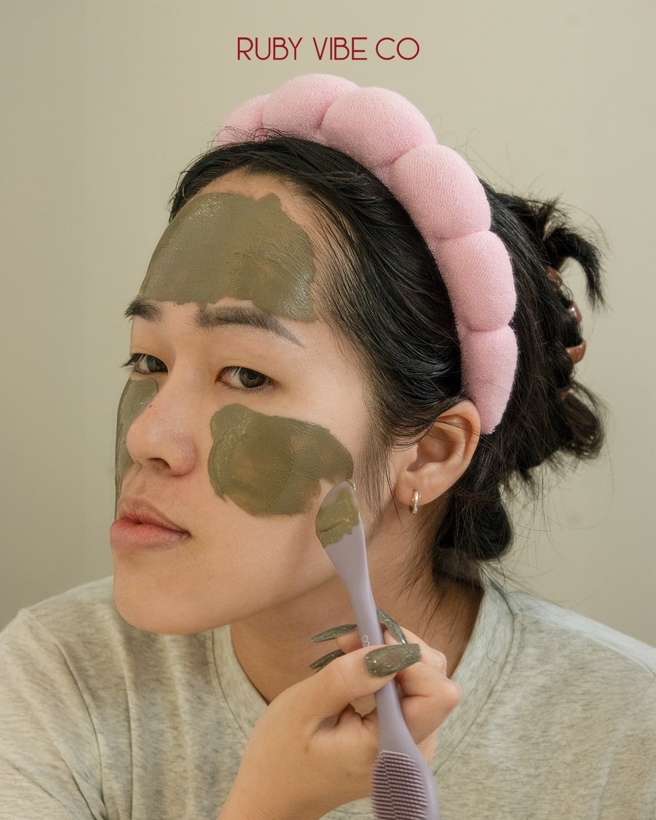 A woman with a pink headband applies a clay mask, a practical image for a guide on what to look for when buying a skincare headband.