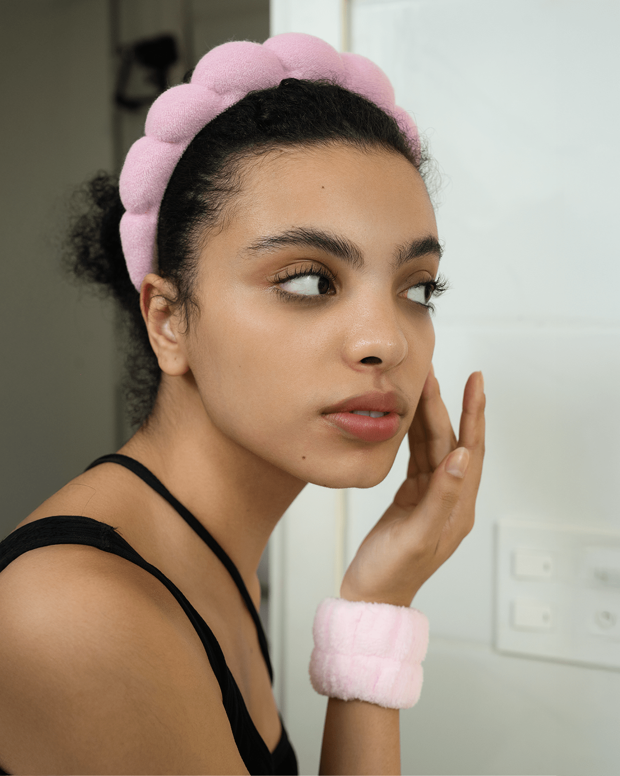 A portrait of a woman wearing a pink puffy headband, demonstrating a key accessory to look for when buying a skincare headband.