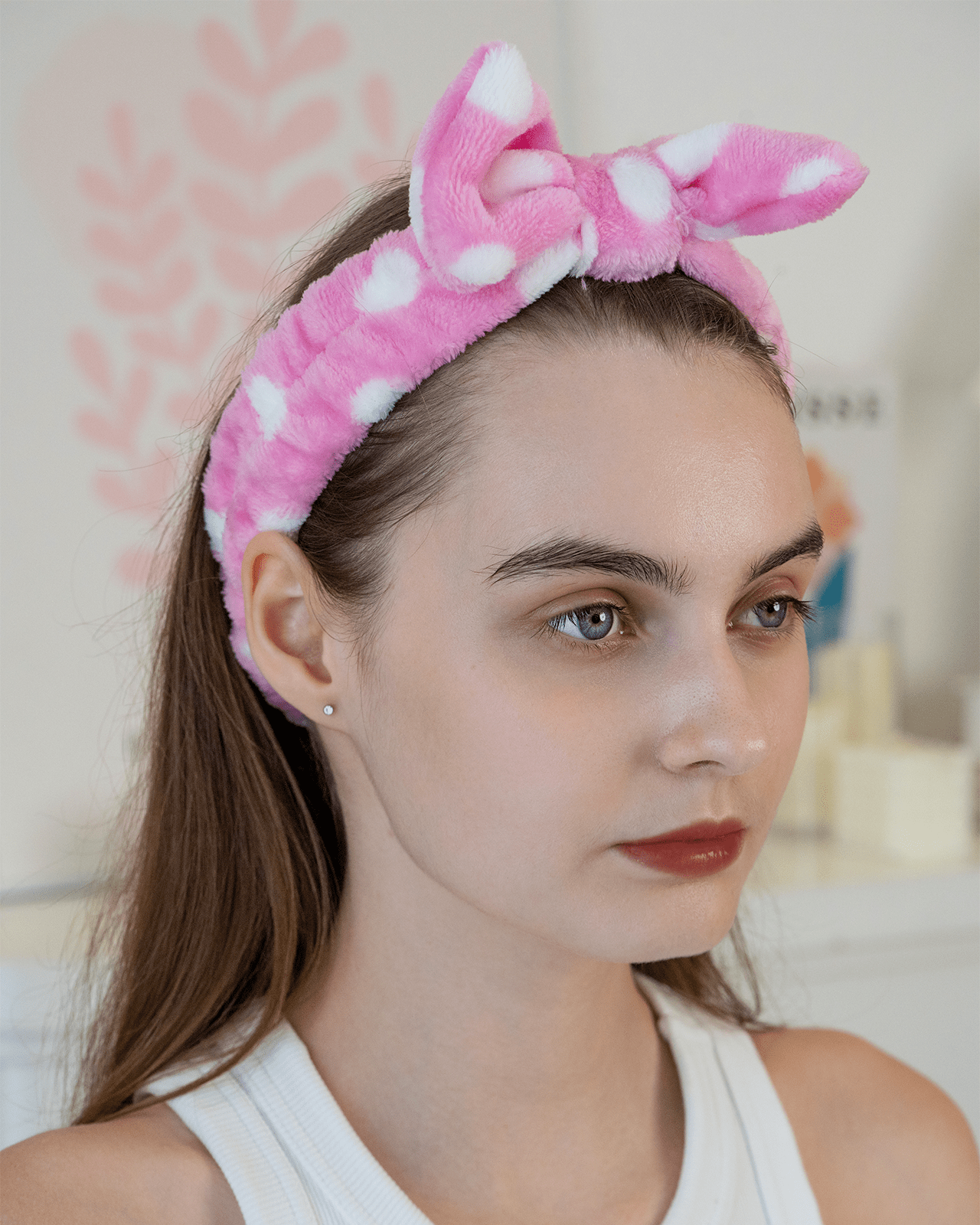 A portrait of a woman wearing a pink, polka-dot headband, demonstrating a stylish accessory to look for in a skincare headband guide.