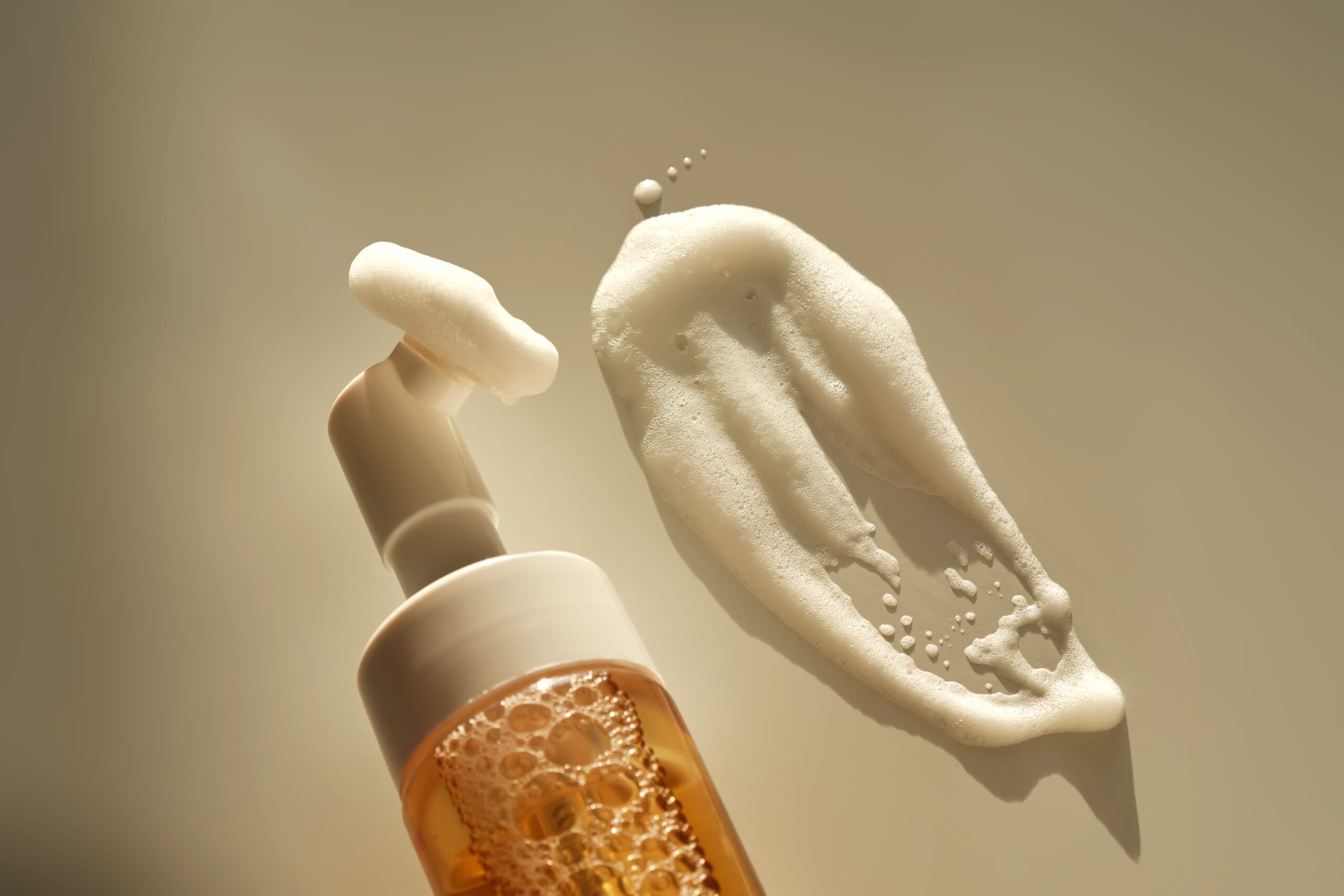 A macro shot of a white foam cleanser being dispensed from a pump bottle, showcasing the texture of a gentle, effective face wash.