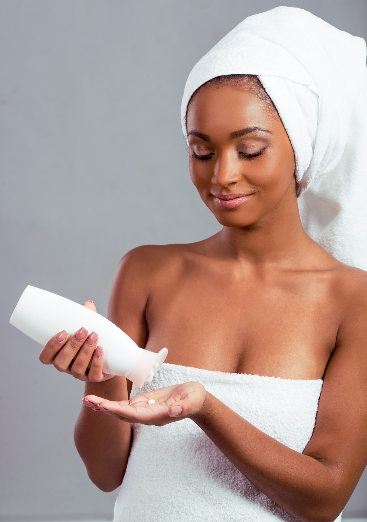 Woman wrapping a plush white towel around her body after bathing, preparing for the next step of moisturizing.