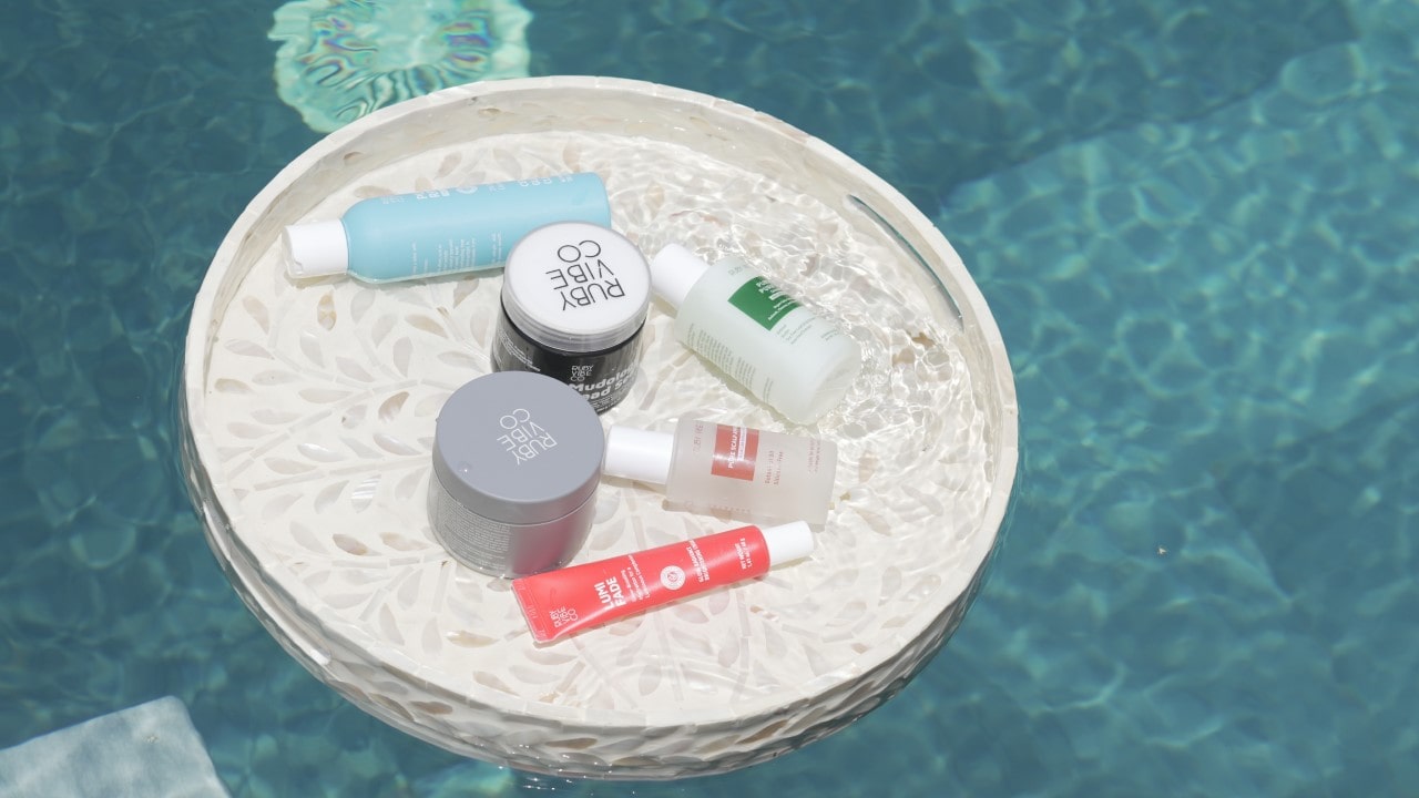 Top-down view of essential body care items like moisturizer, body scrub, and serum laid out on a clean, bright surface.