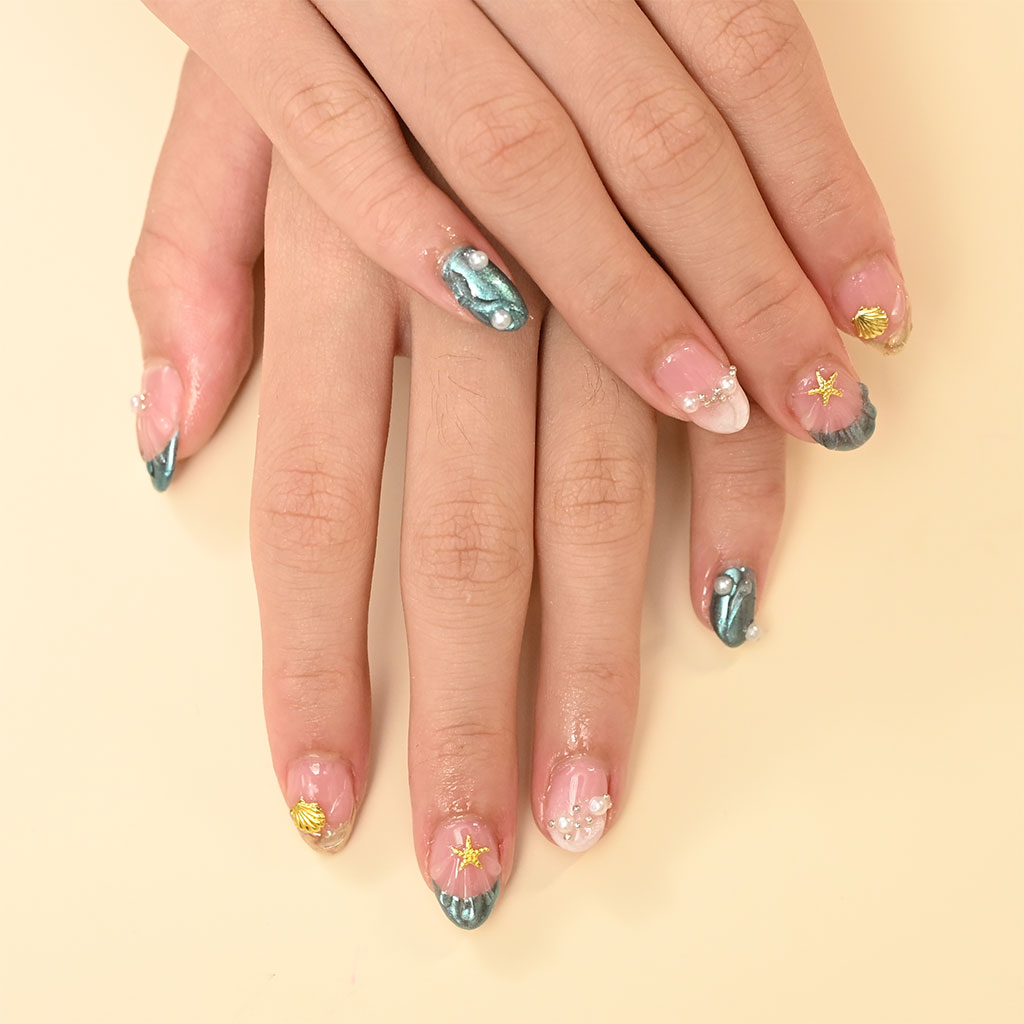 An ocean-themed manicure with turquoise cat-eye nails, clear extensions, and embellishments like pearls, gold seashells, and starfish charms.