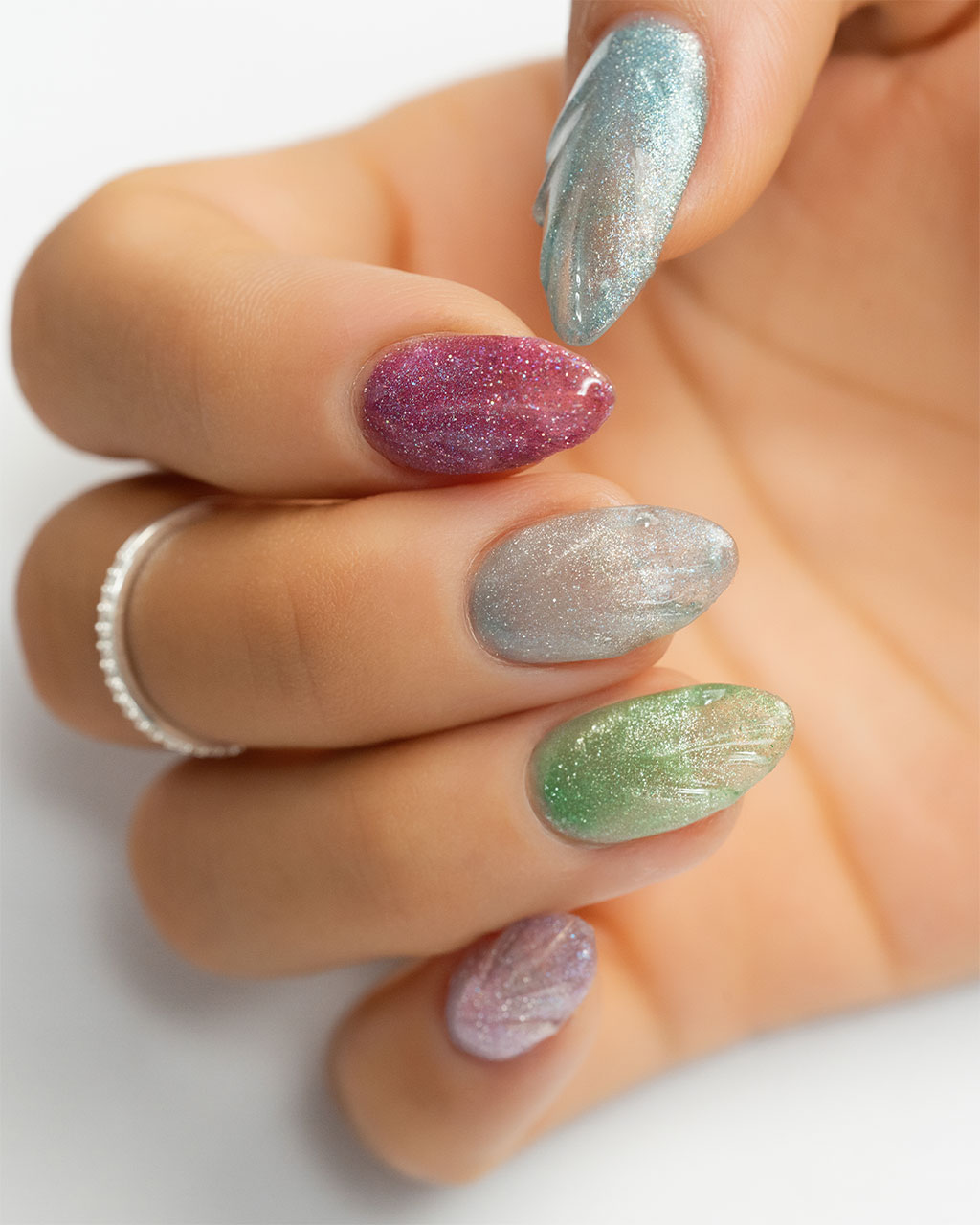 A hand displaying a colorful manicure with each nail painted in a different shade of sparkling holographic polish.
