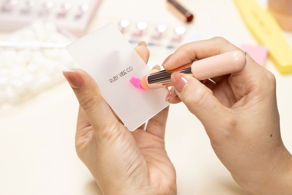 A person uses a pink sponge-tipped tool to blend pink and orange nail polish on a frosted plastic palette in preparation for creating an ombre nail design.